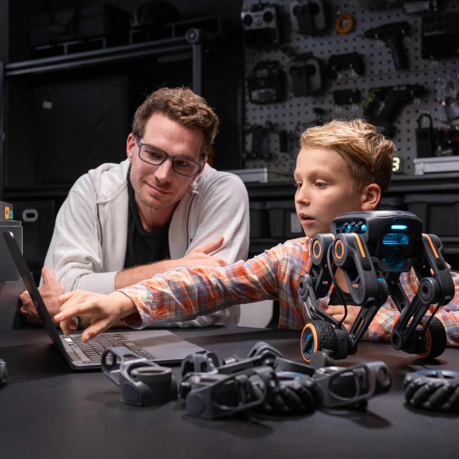 Man and boy looking at a laptop, a robotic toy is on the table. Workshop background.