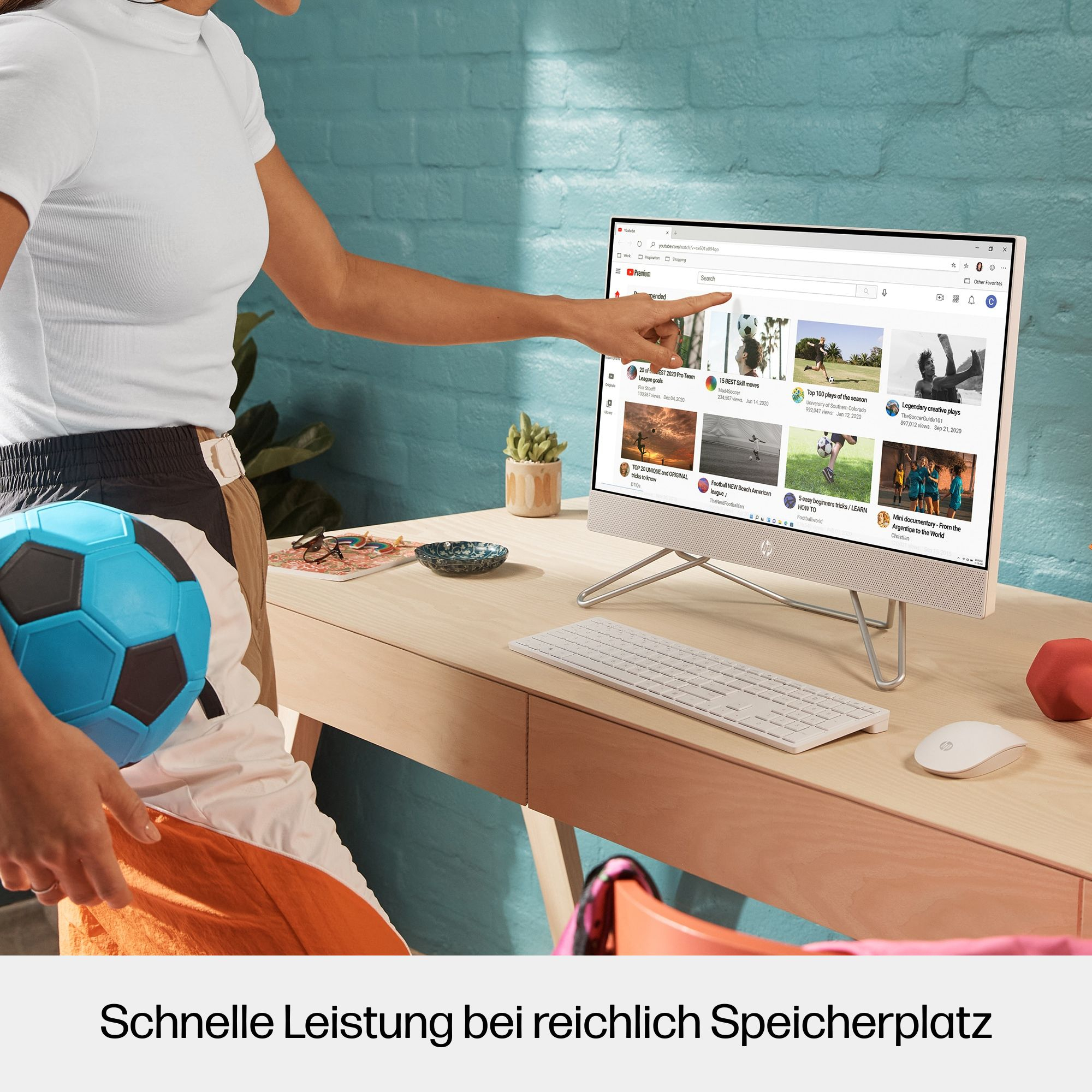 Eine Person zeigt auf einen Computerbildschirm. Ein Fußball und andere Gegenstände sind in der Nähe.