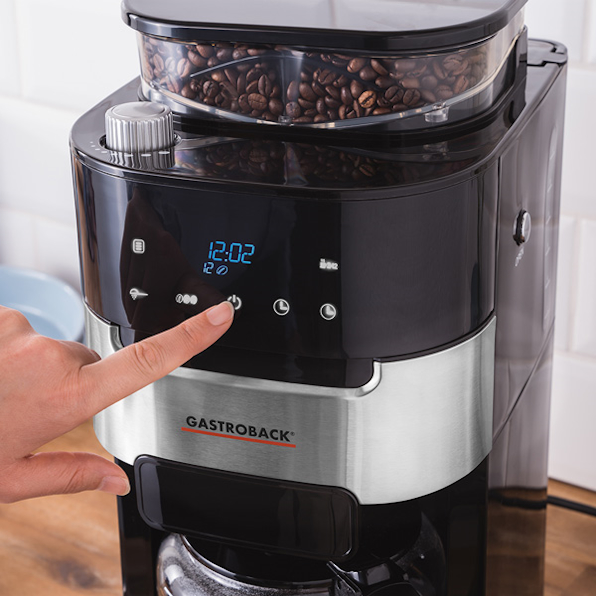 Palec osoby naciskający przycisk zasilania czarnego ekspresu do kawy. Wyświetlacz pokazuje godzinę.