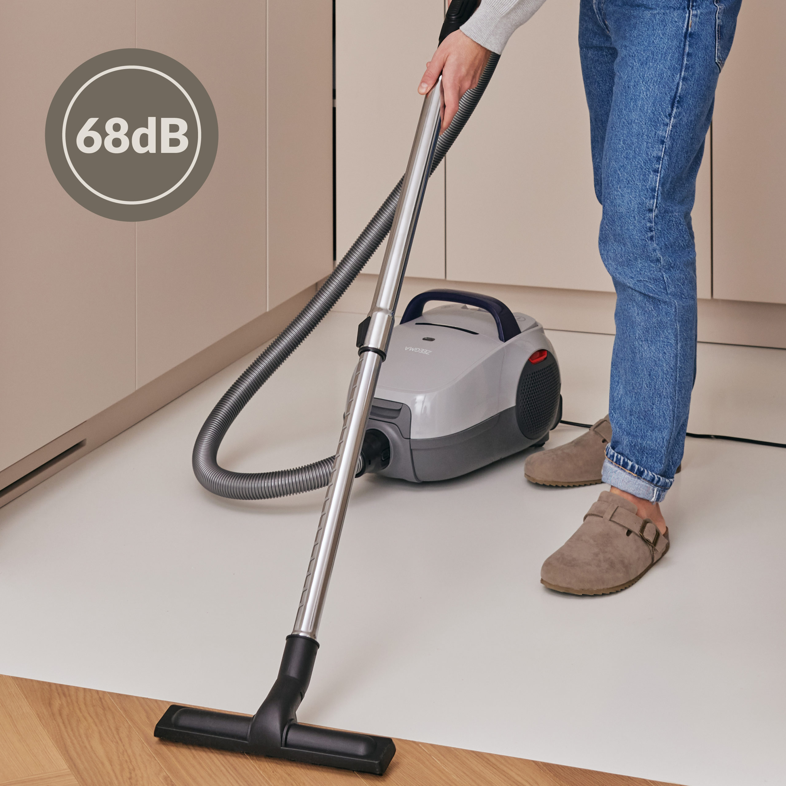 Osoba odkurzająca podłogę. Odkurzacz jest szary, ze wskaźnikiem poziomu hałasu 68 dB.