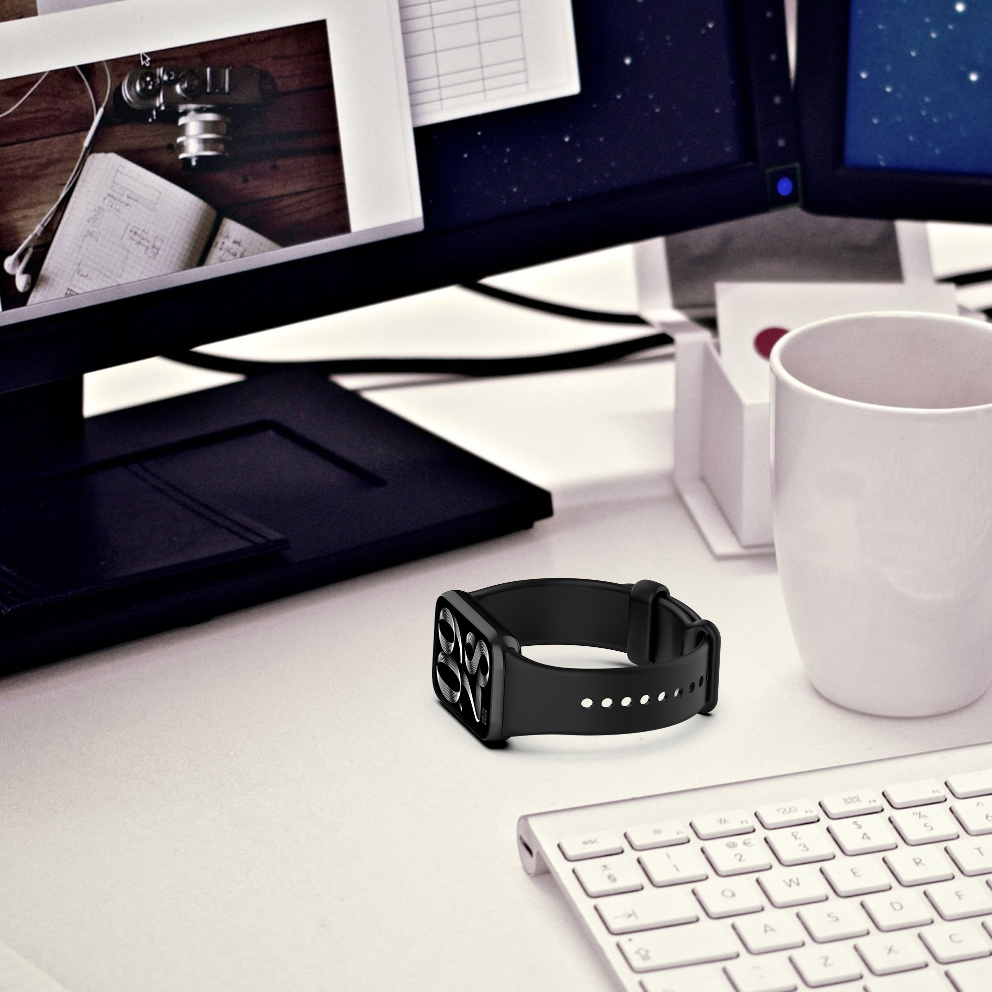 Ein schwarzes Apple Watch-Armband auf einem weißen Schreibtisch, in der Nähe einer Tastatur und eines Monitors, mit einem weißen Becher.