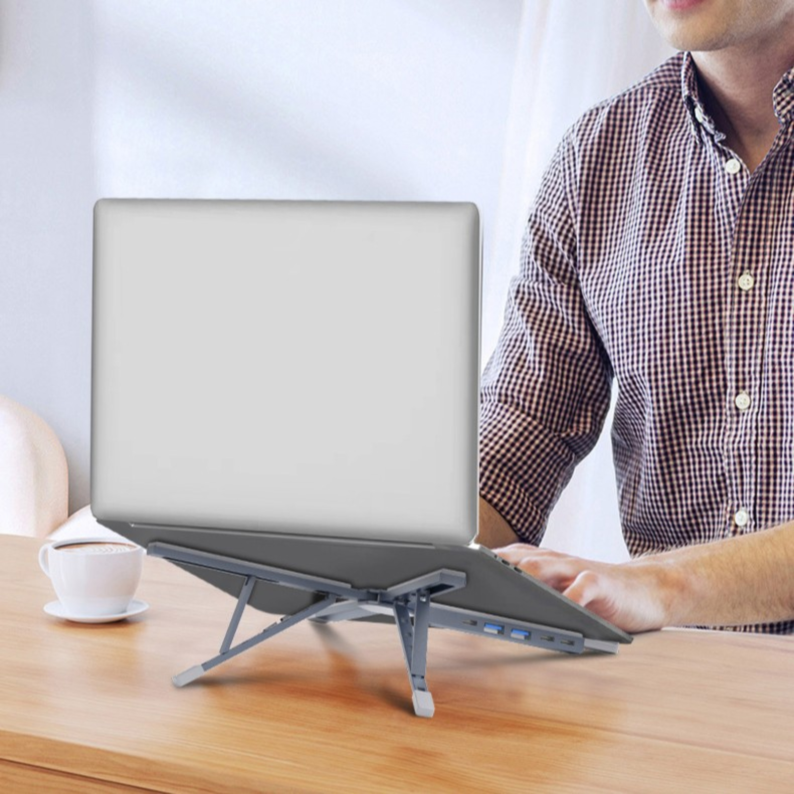 Ein Mann benutzt einen Laptop auf einem faltbaren grauen Ständer auf einem Holztisch.