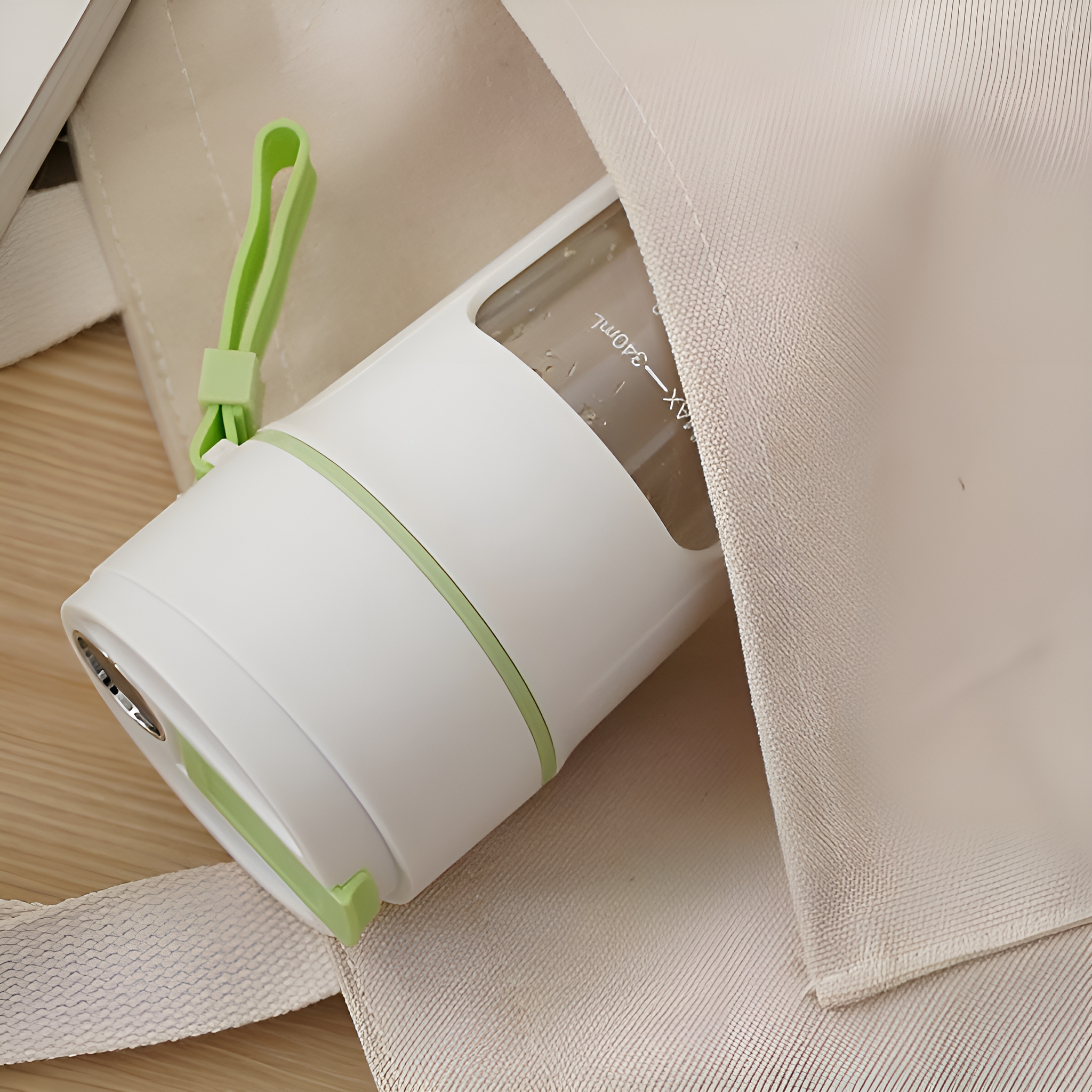 Ein weißer und grüner tragbarer Mixer, teilweise in einer Canvas-Tasche. Ein Buch ist im Hintergrund.