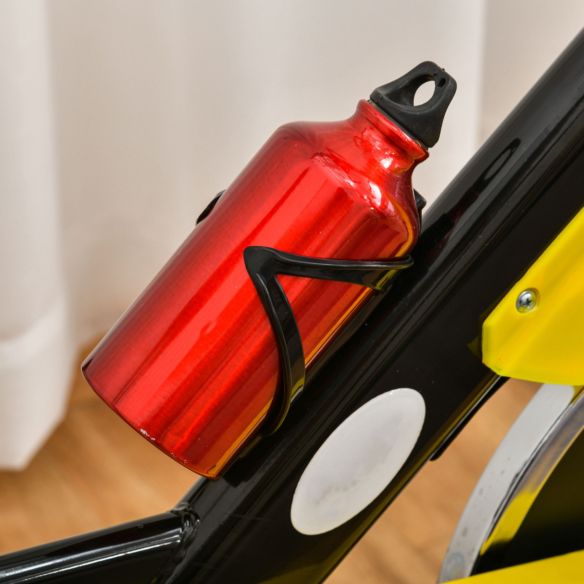 Eine rote Wasserflasche in einem schwarzen Halter ist an einem stationären Fahrrad befestigt.