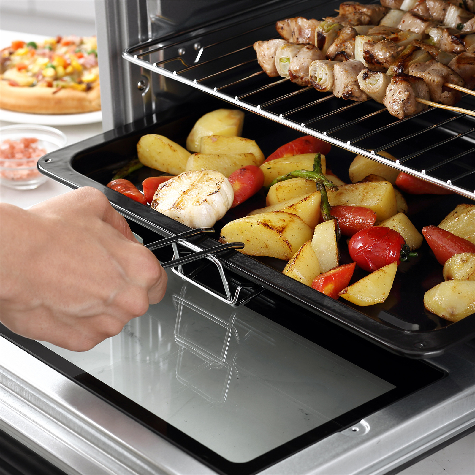 Backofen mit Essen darin. Eine Hand zieht das Tablett mit gebratenen Kartoffeln und Gemüse heraus.