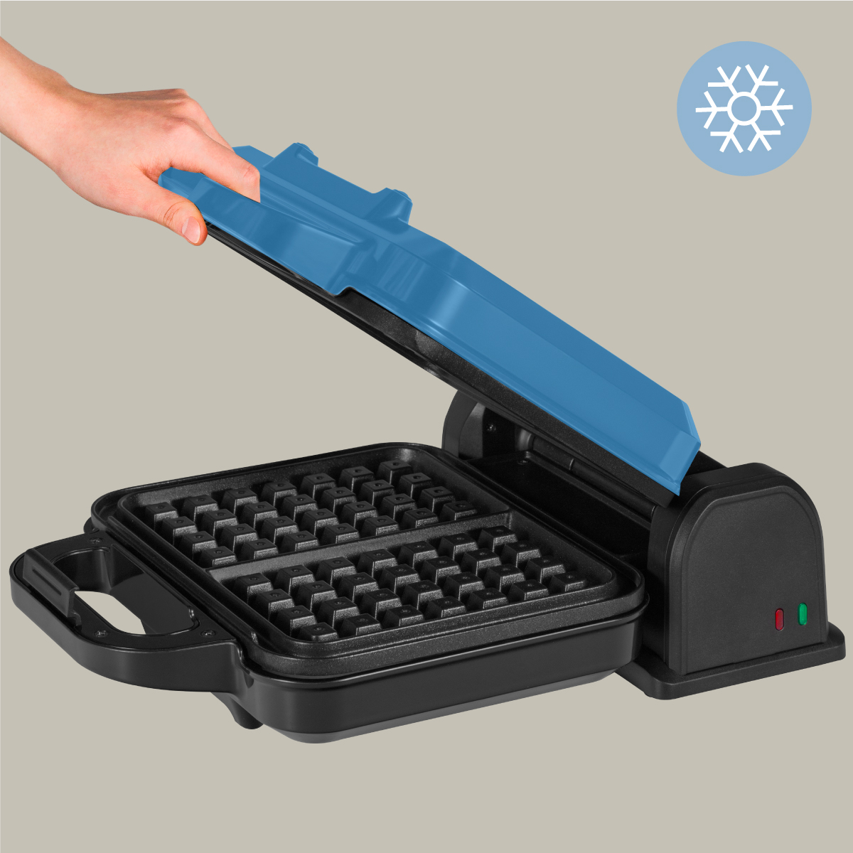 Gofrownica z niebieską pokrywą, otwarta, odsłaniająca kratki do gofrów i dłoń.