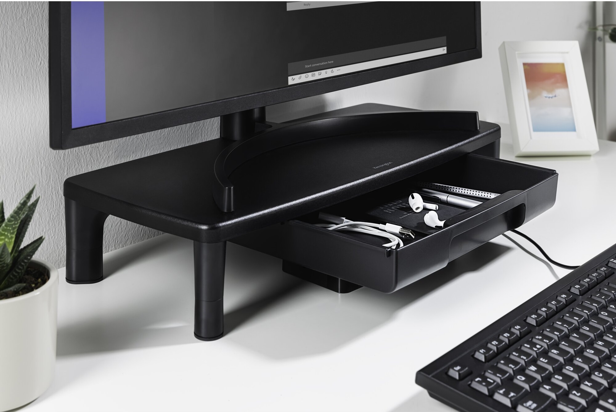 Schwarzer Monitorständer mit Schublade. Ein Monitor sitzt oben mit einer Tastatur und Maus darunter auf einem weißen Schreibtisch.