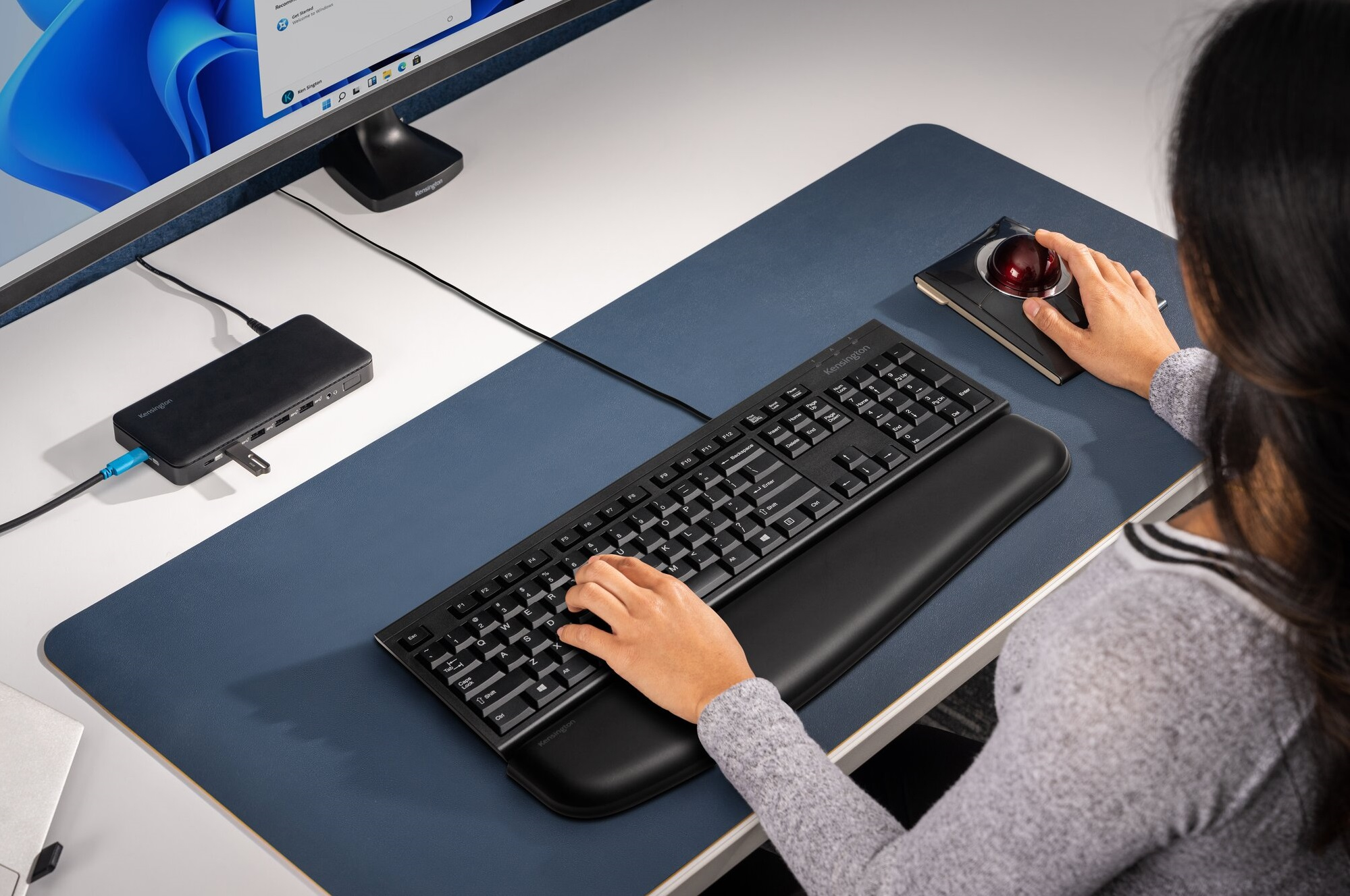 Frau benutzt Tastatur und Trackball-Maus auf einem Schreibtisch mit blauer Matte.