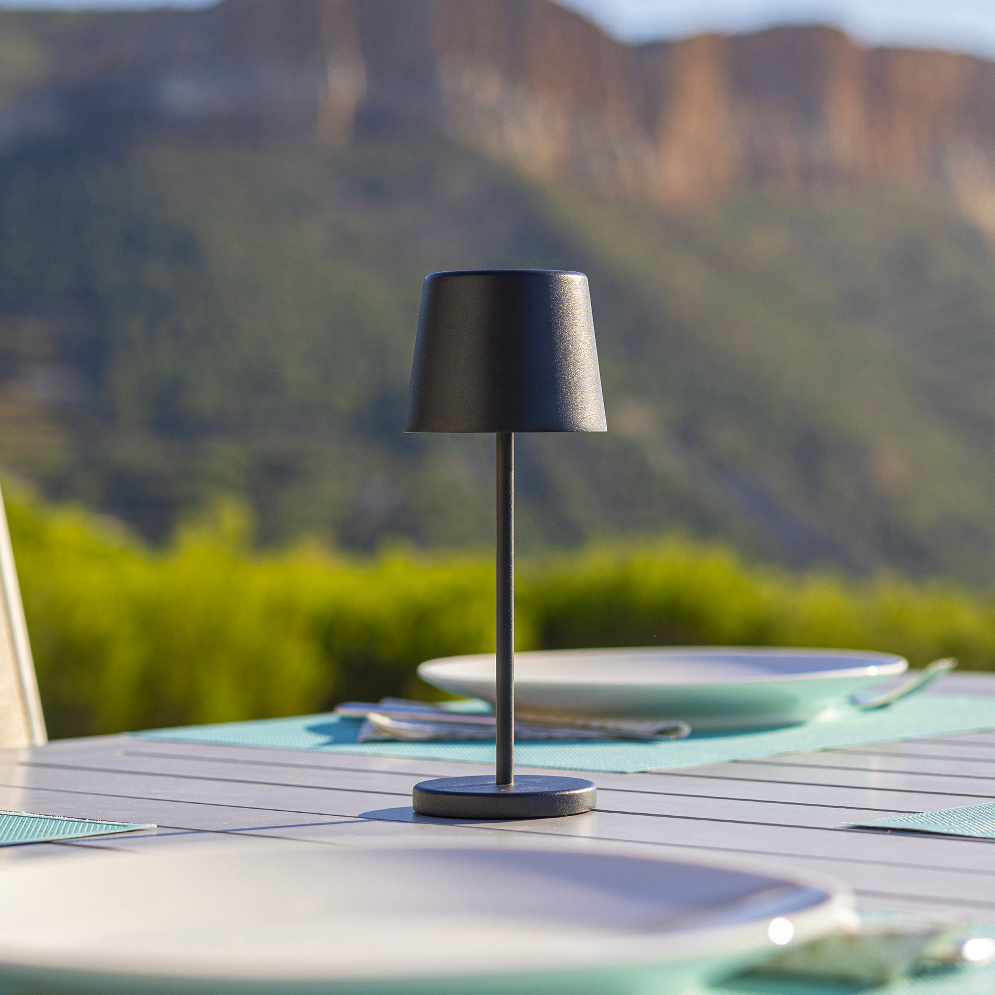 Schwarze Außenlampe auf einem Tisch. Der Hintergrund zeigt einen Berg und grüne Vegetation.