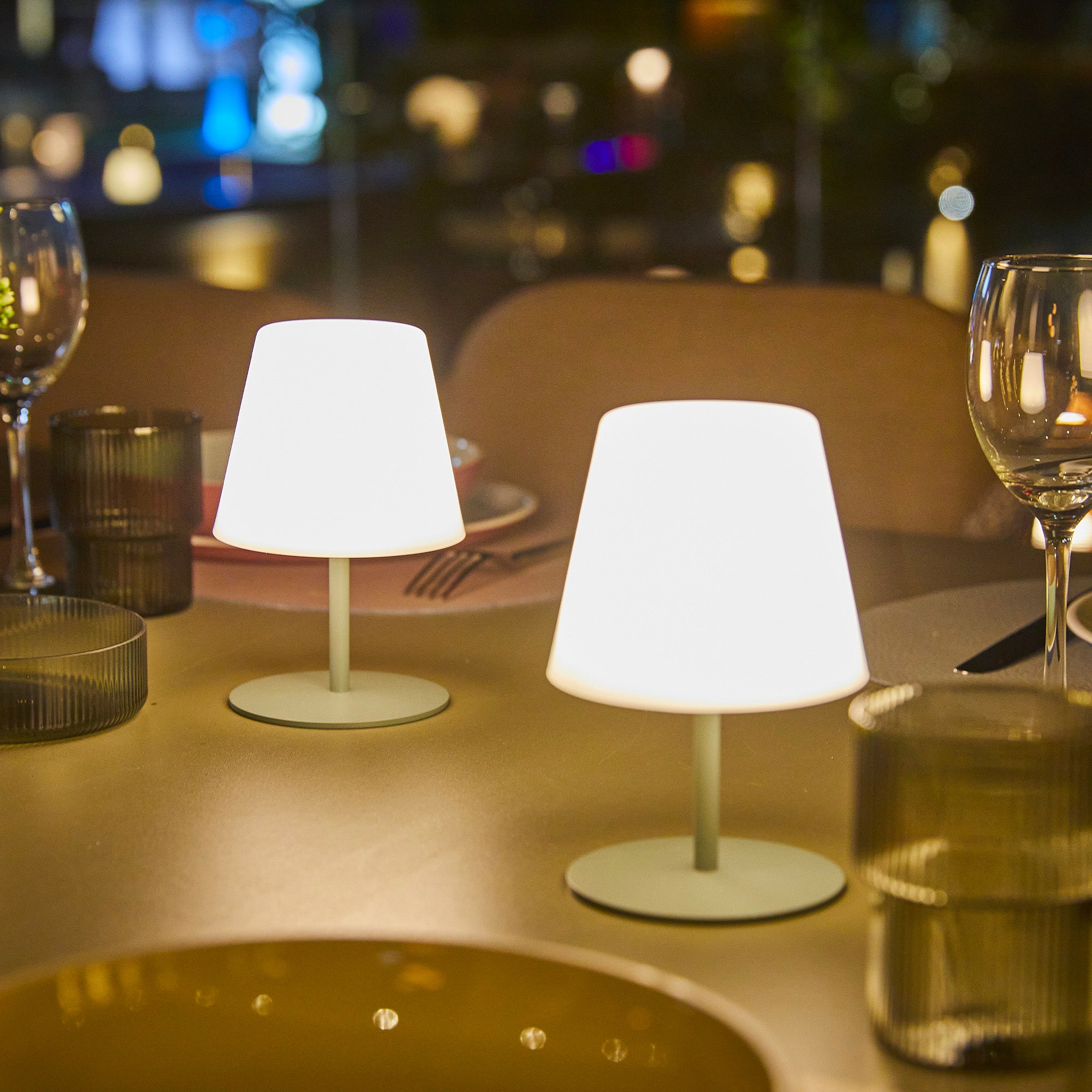 Zwei weiße Tischlampen mit grünen Sockeln auf einem Tisch, Restaurant-Setting.