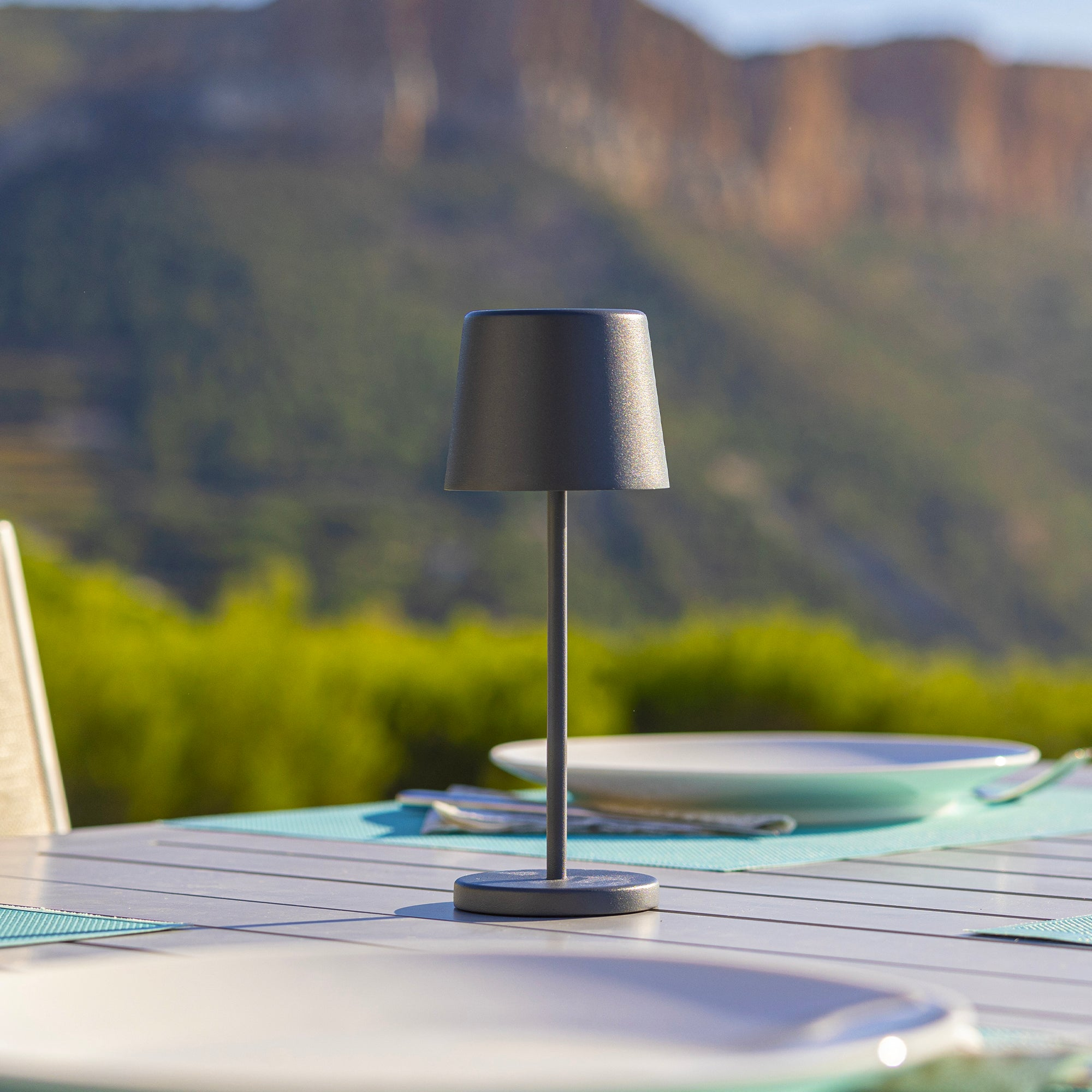 Eine schwarze Außenlampe auf einem Tisch mit Blick auf Berge und Himmel im Hintergrund.