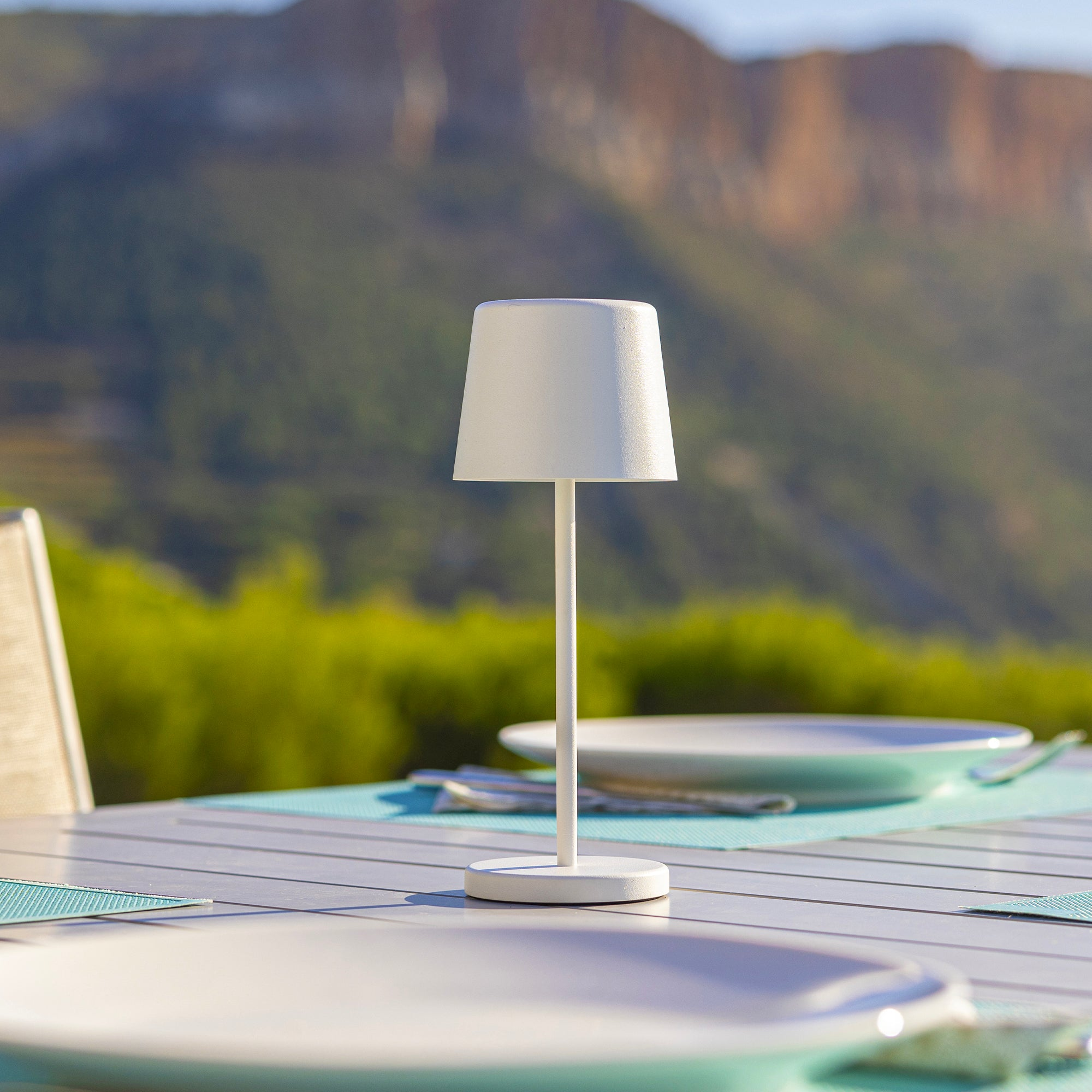 Eine weiße Lampe auf einem Tisch mit Tellern, mit Bergen im Hintergrund.