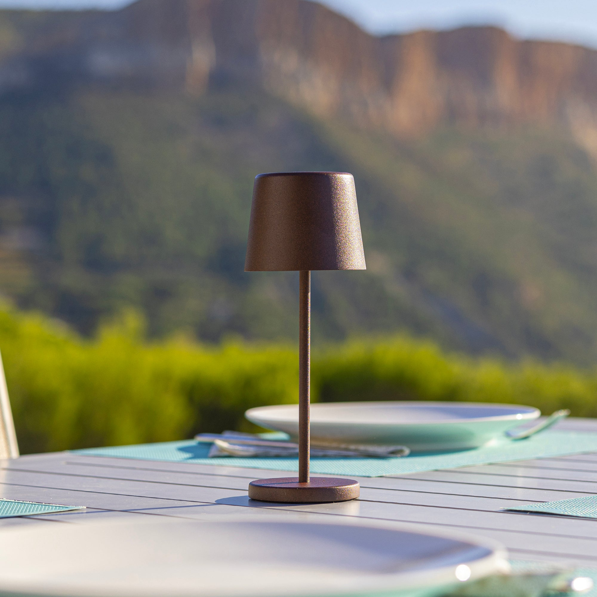 Braune Lampe auf Tisch mit Tellern und Bergblick im Hintergrund.