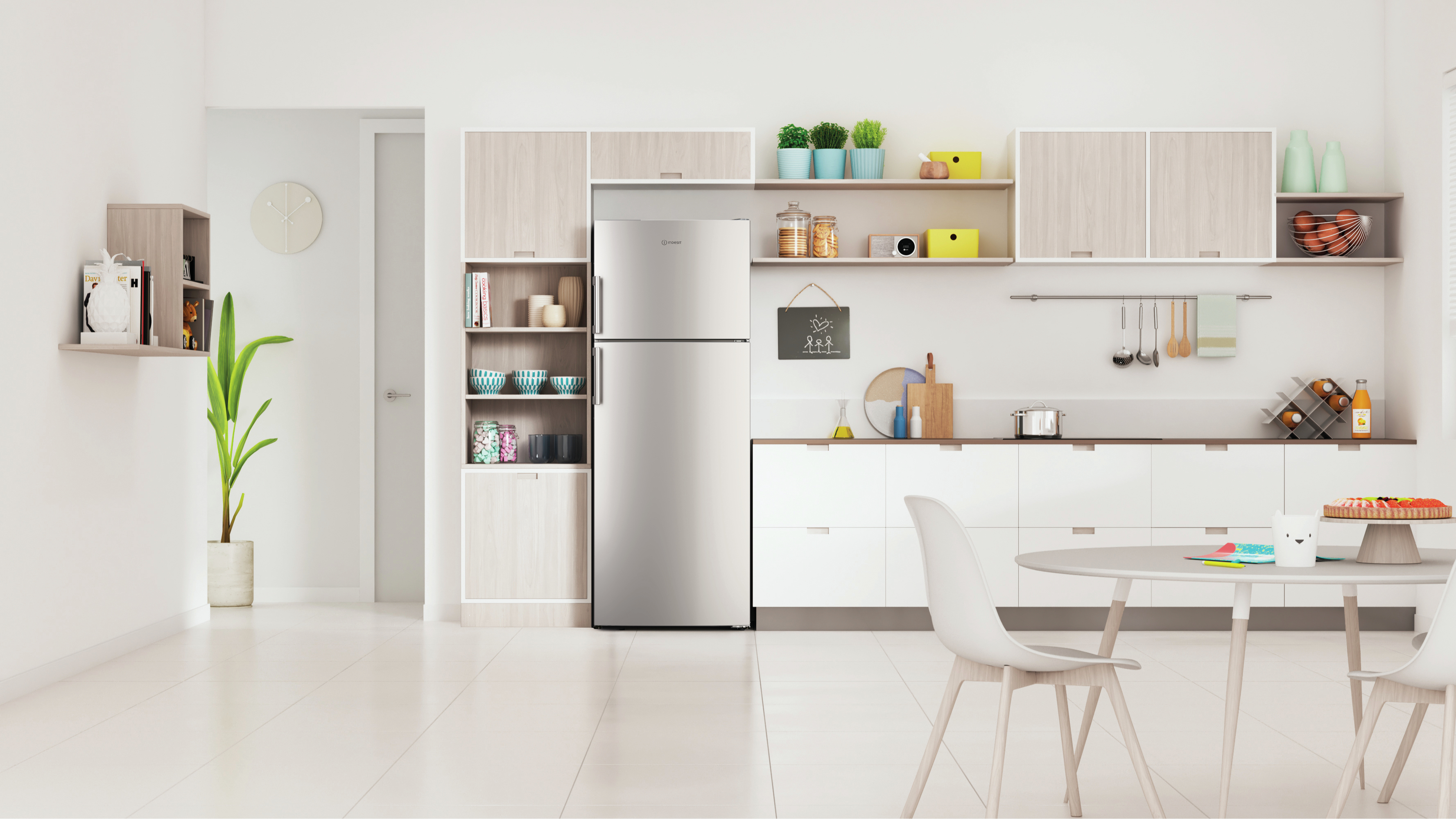 Cucina moderna con mobili bianchi, frigorifero in acciaio inox e tavolo rotondo con sedie. Piante e decorazioni sugli scaffali.