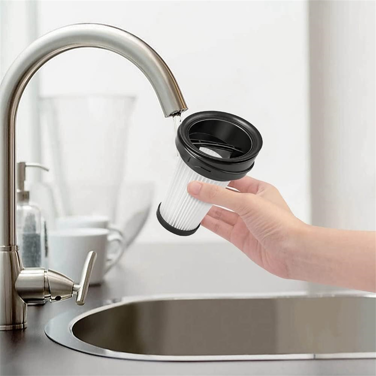 Eine Hand spült einen Staubsaugerfilter unter einem laufenden Wasserhahn ab.