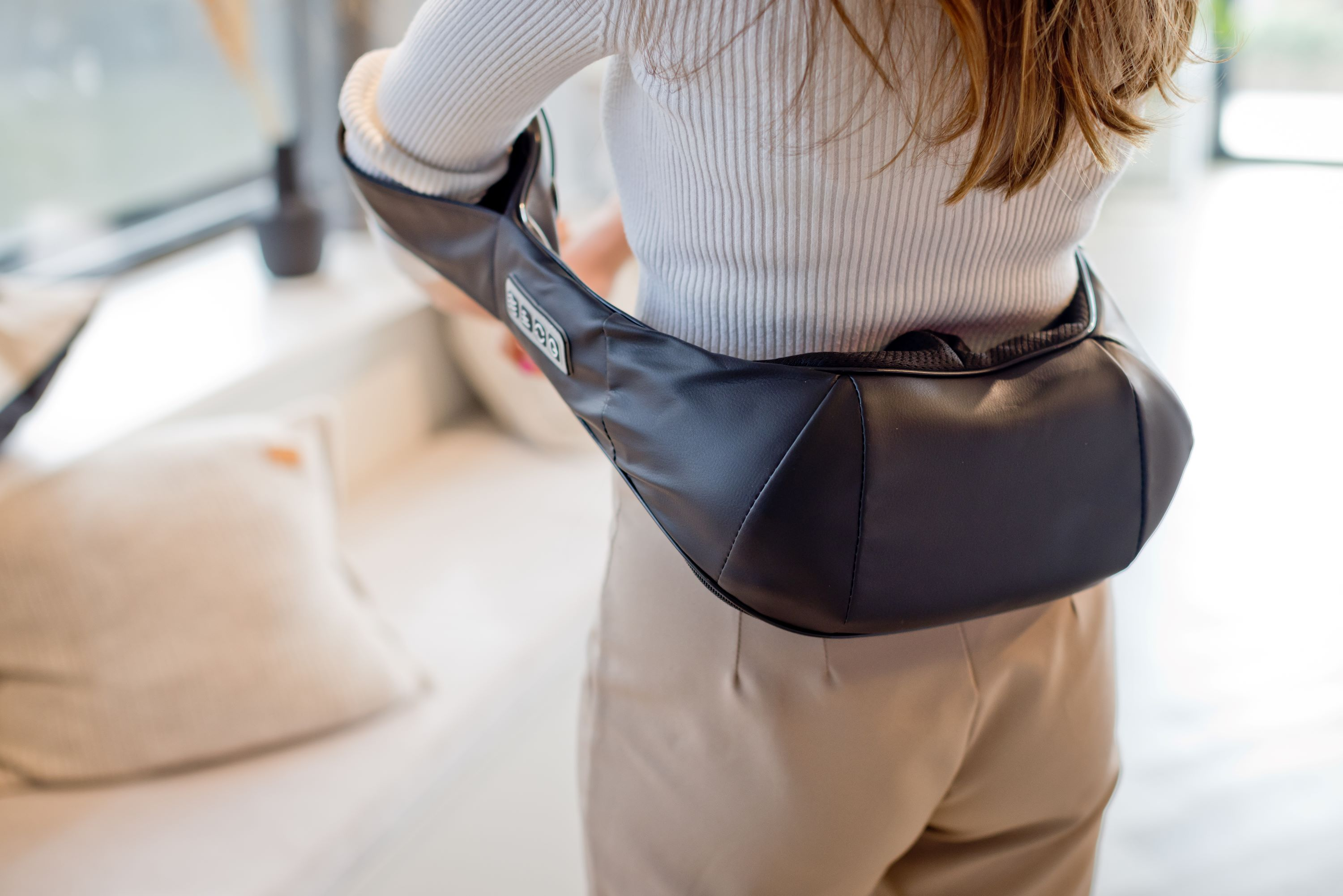 A person from the back wearing a black massage device around their shoulders.