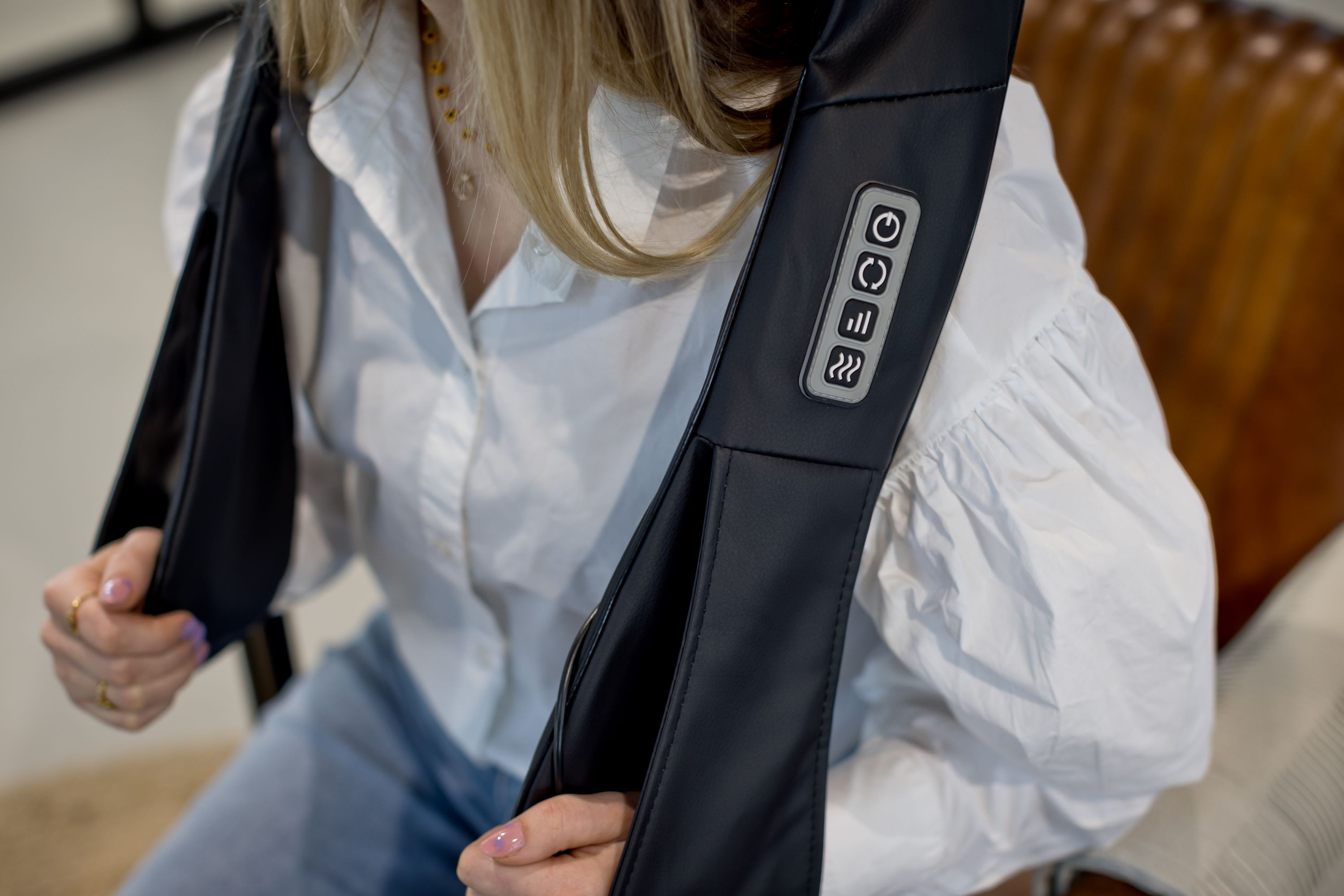 Woman wearing black massage device. White shirt. Buttons visible. Blurred background.