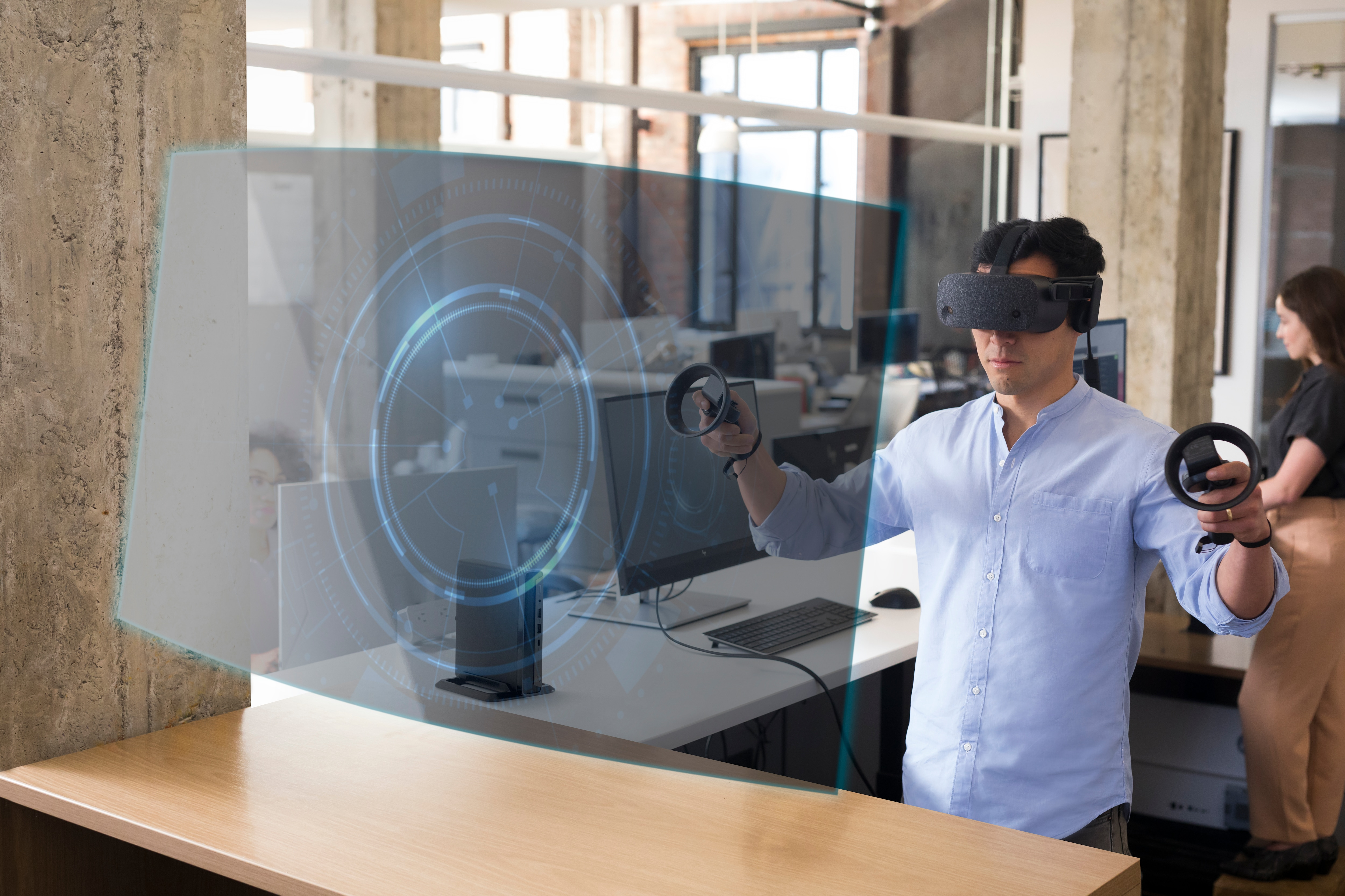 Uomo con visore VR e controller, interagisce con display olografico blu.