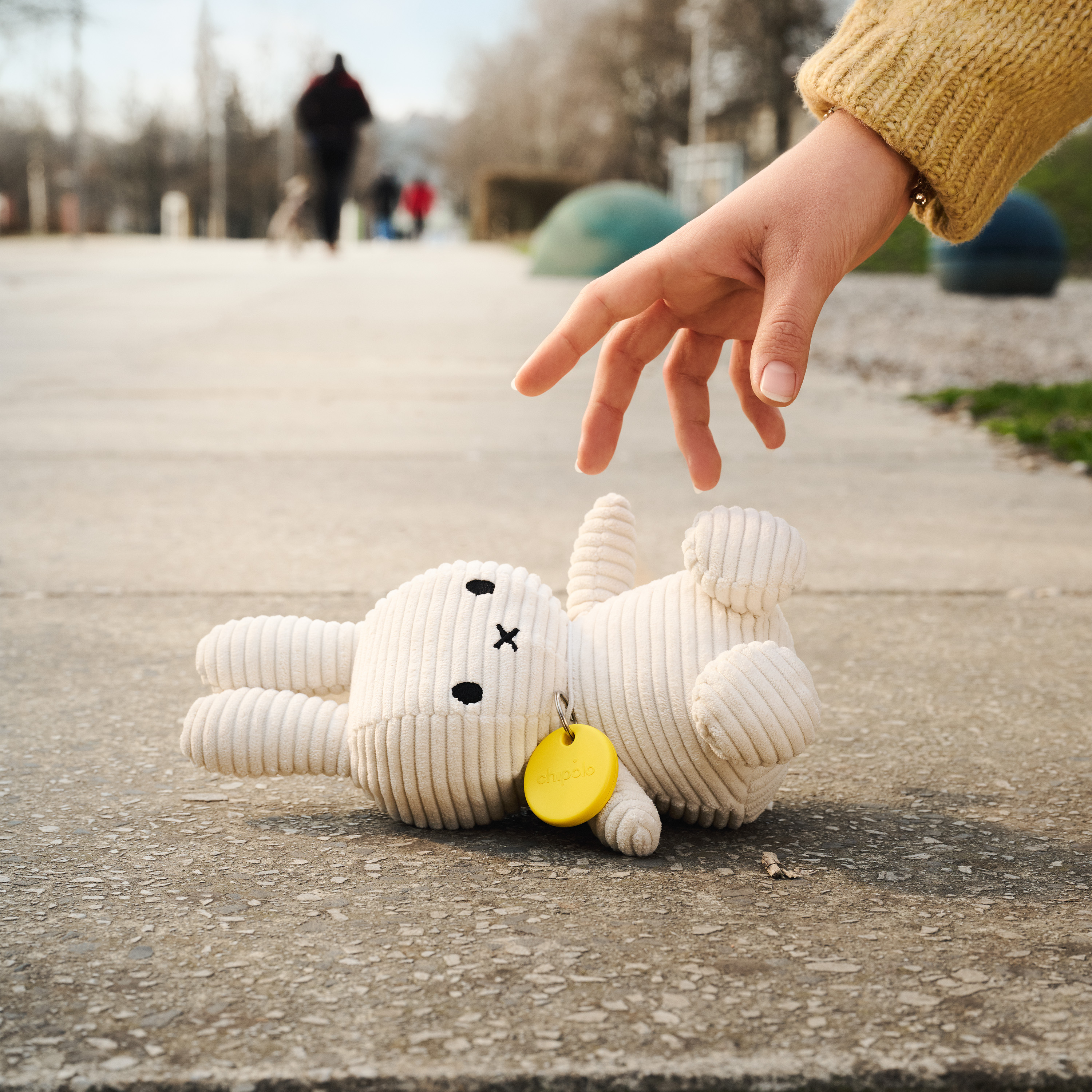 A child's hand reaching towards a white toy rabbit lying on a concrete surface.