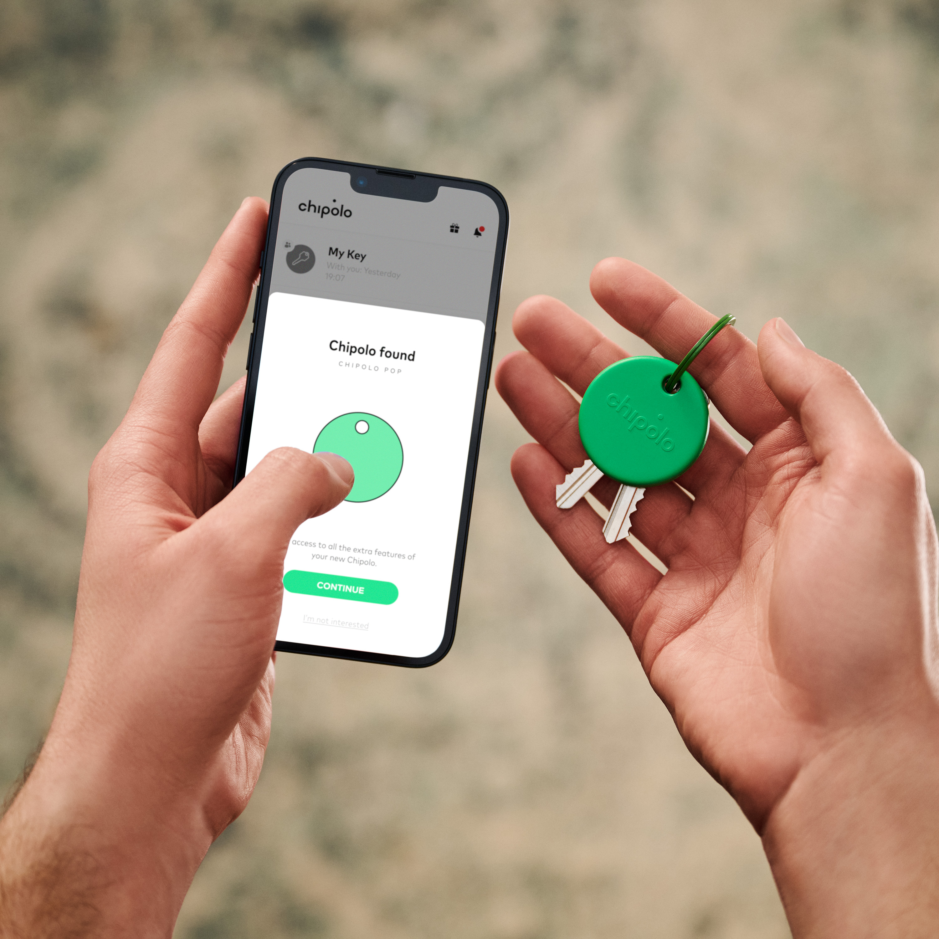 Hands holding a phone showing Chipolo found and a green Chipolo on keys.