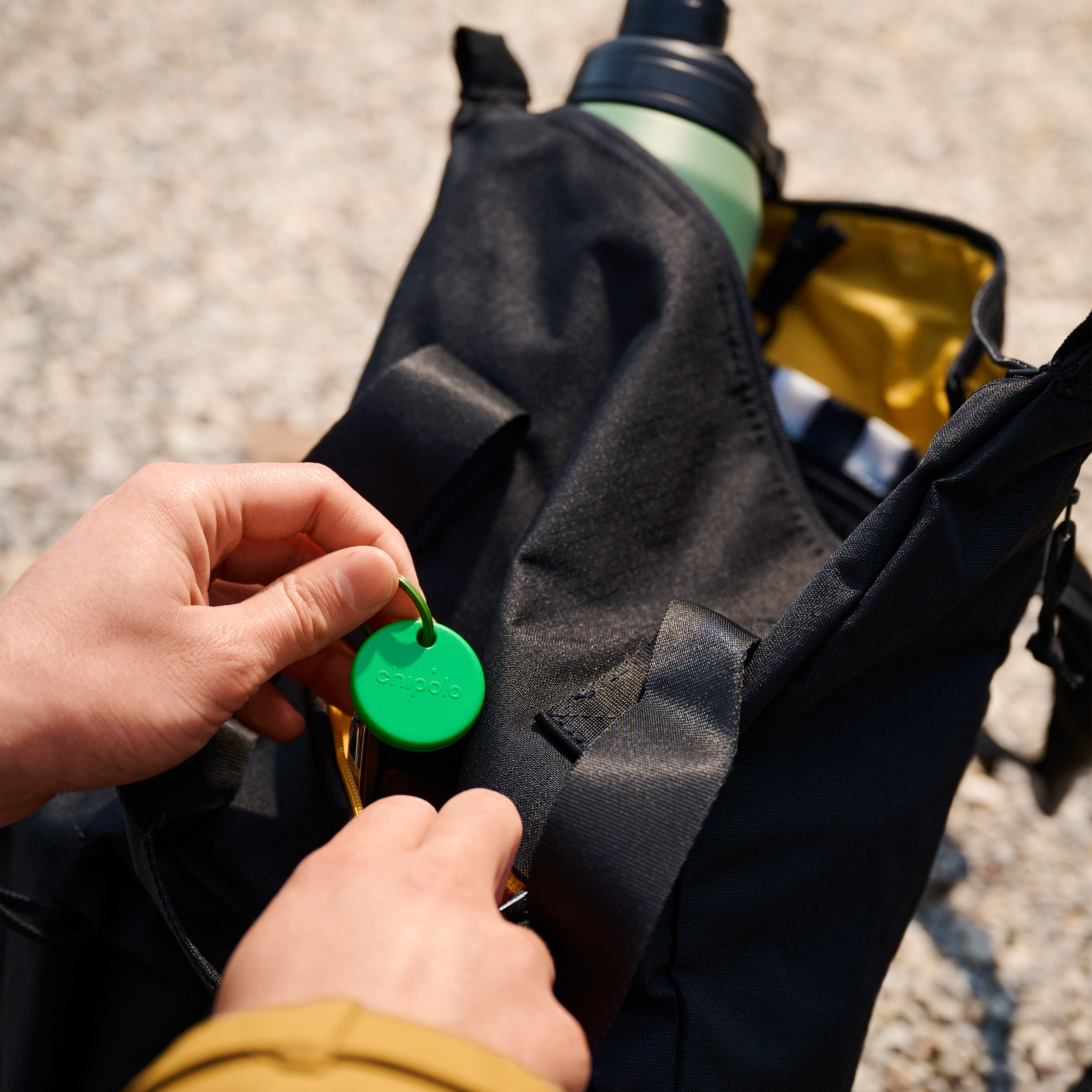 Person's hands holding a green Chipolo device. The device is in a black bag.
