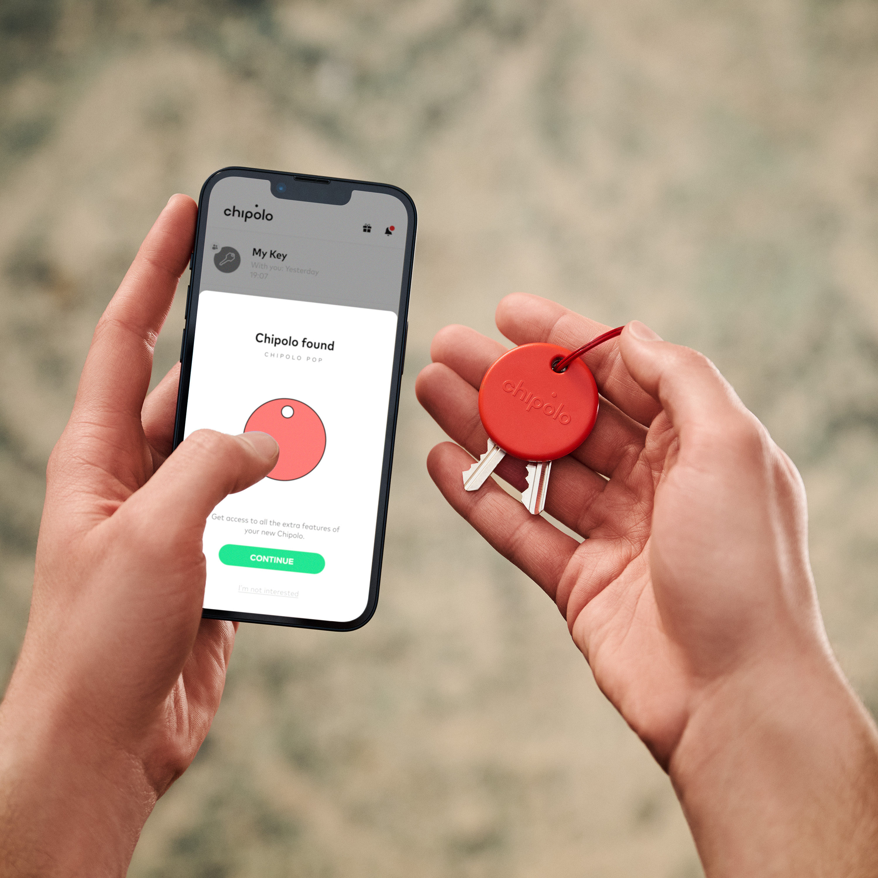 Een persoon die een telefoon vasthoudt met een sleutelzoeker-app en rode sleutelhangers.