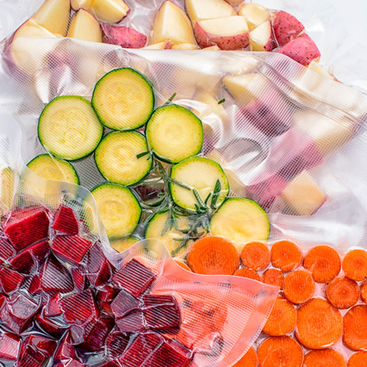 Różne warzywa w przezroczystych workach pakowanych próżniowo, w tym buraki, marchew i cukinia.