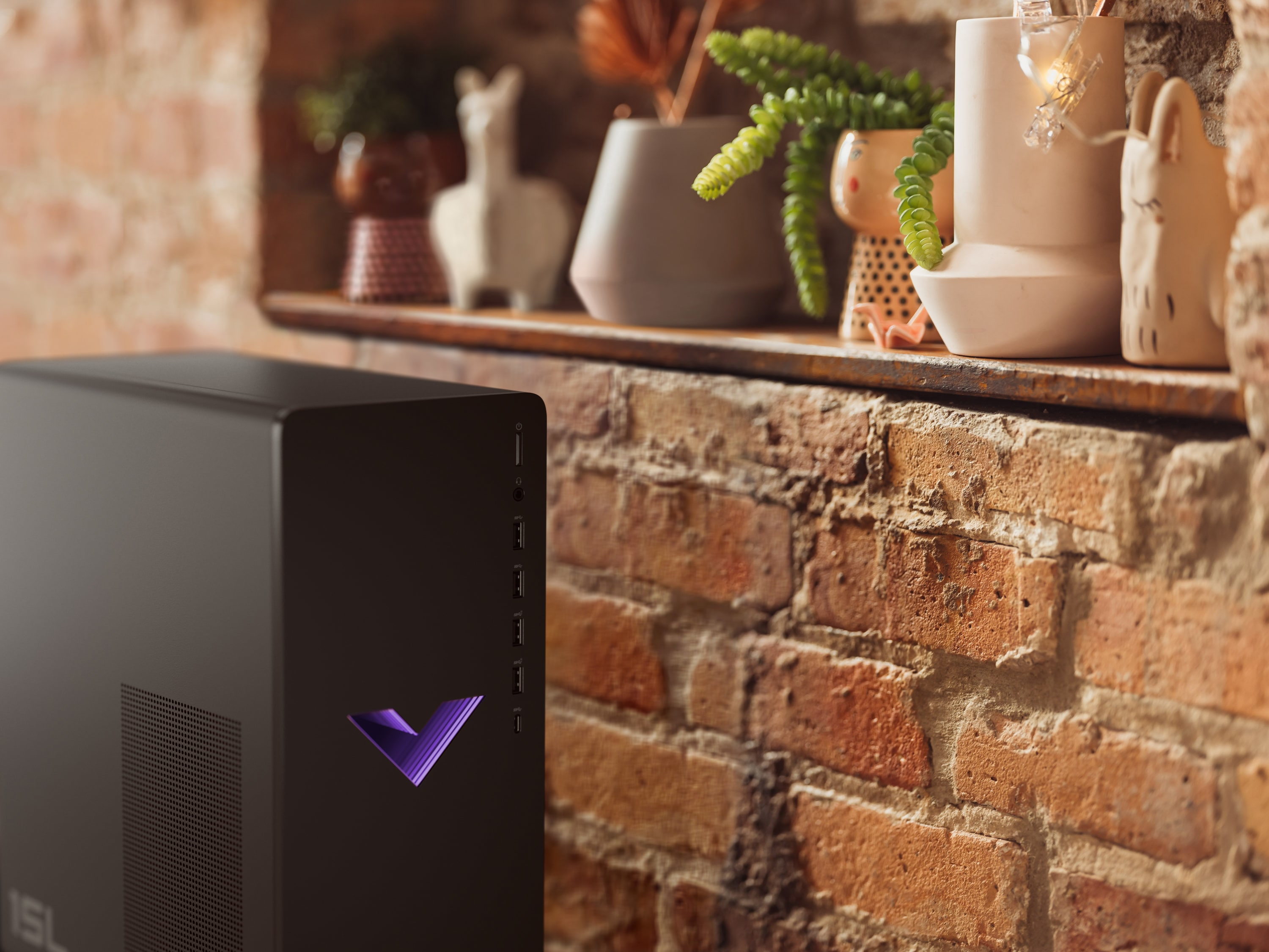 Czarna wieża komputera z fioletowym logo V, umieszczona na ceglanej półce. Widoczne są rośliny i dekoracje.