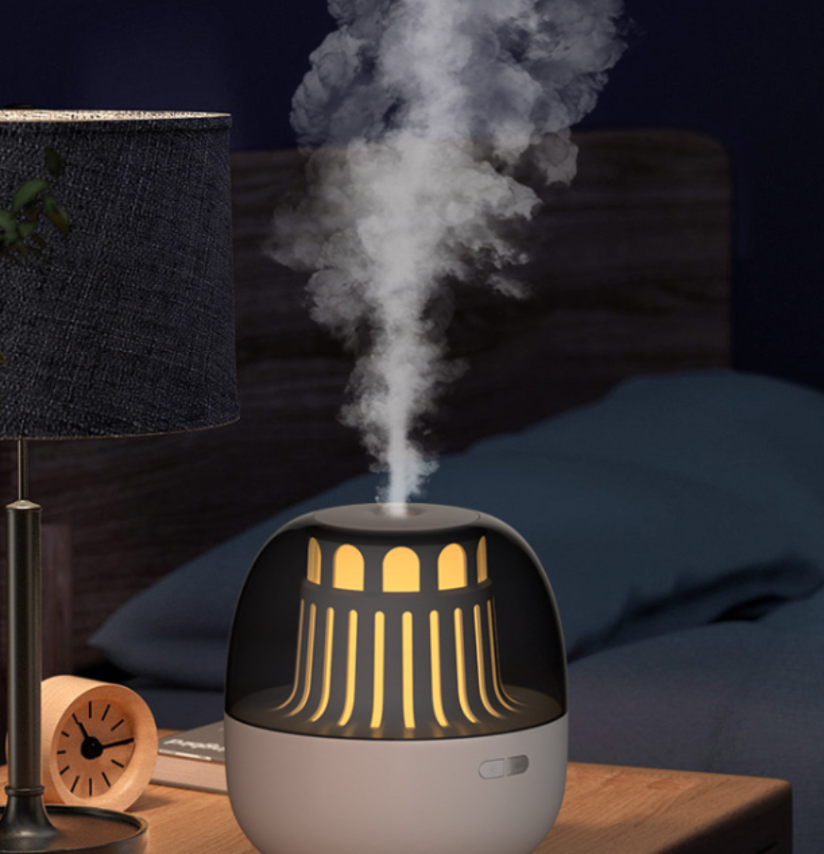Ein weiß-grauer Luftbefeuchter, der Dampf abgibt. Eine Lampe und eine Uhr stehen auf dem Nachttisch.