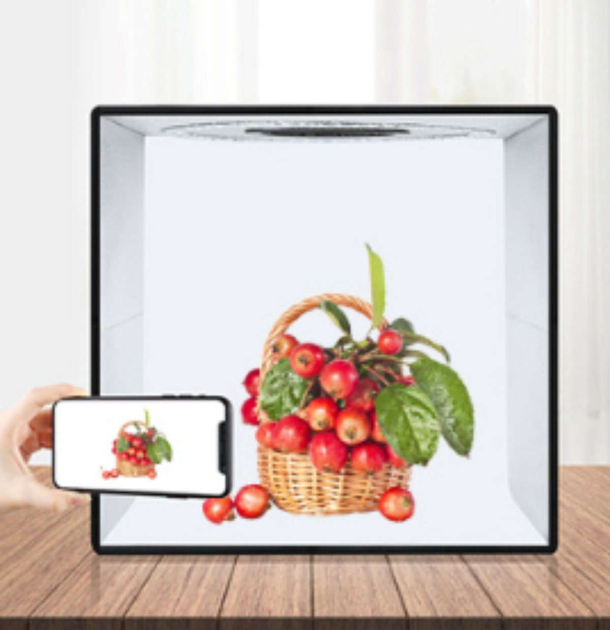 Eine kleine Produktfotografie-Box mit einem Korb roter Äpfel, ein Telefon zeigt dasselbe.