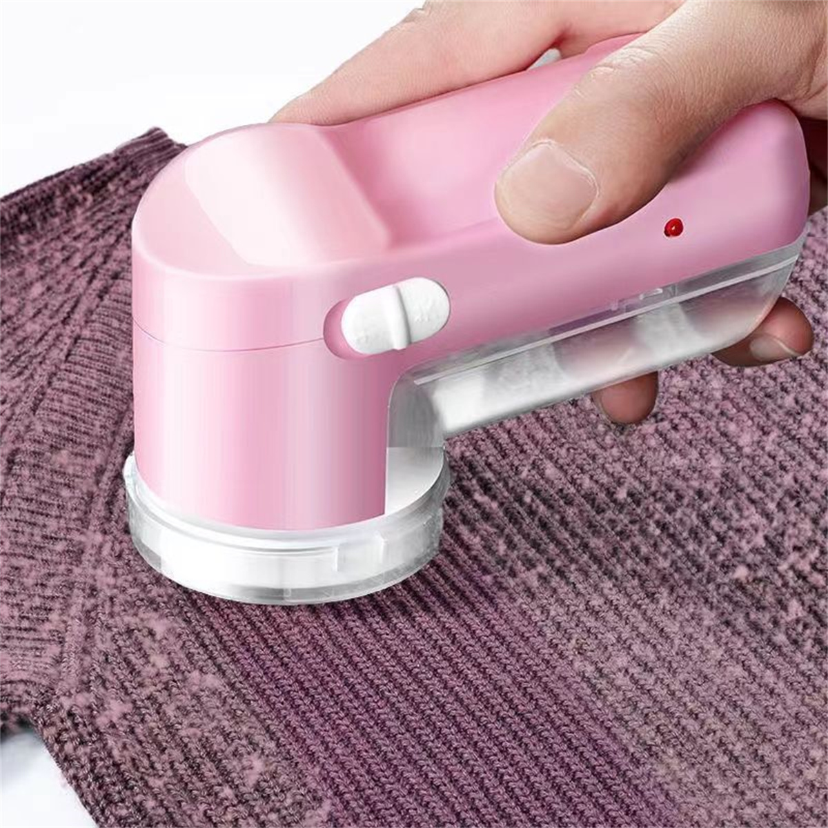 Ein rosa Stoffrasierer entfernt Fusseln von einem lila Pullover, der von einer Hand gehalten wird.