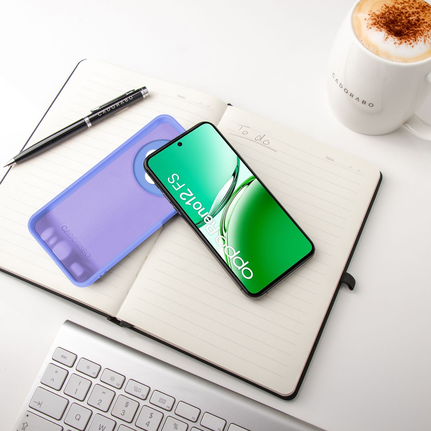 Handyhülle, Telefon, Notizbuch, Stift und Kaffeetasse auf weißer Oberfläche. Das Telefon zeigt Oppo Reno12 FS.