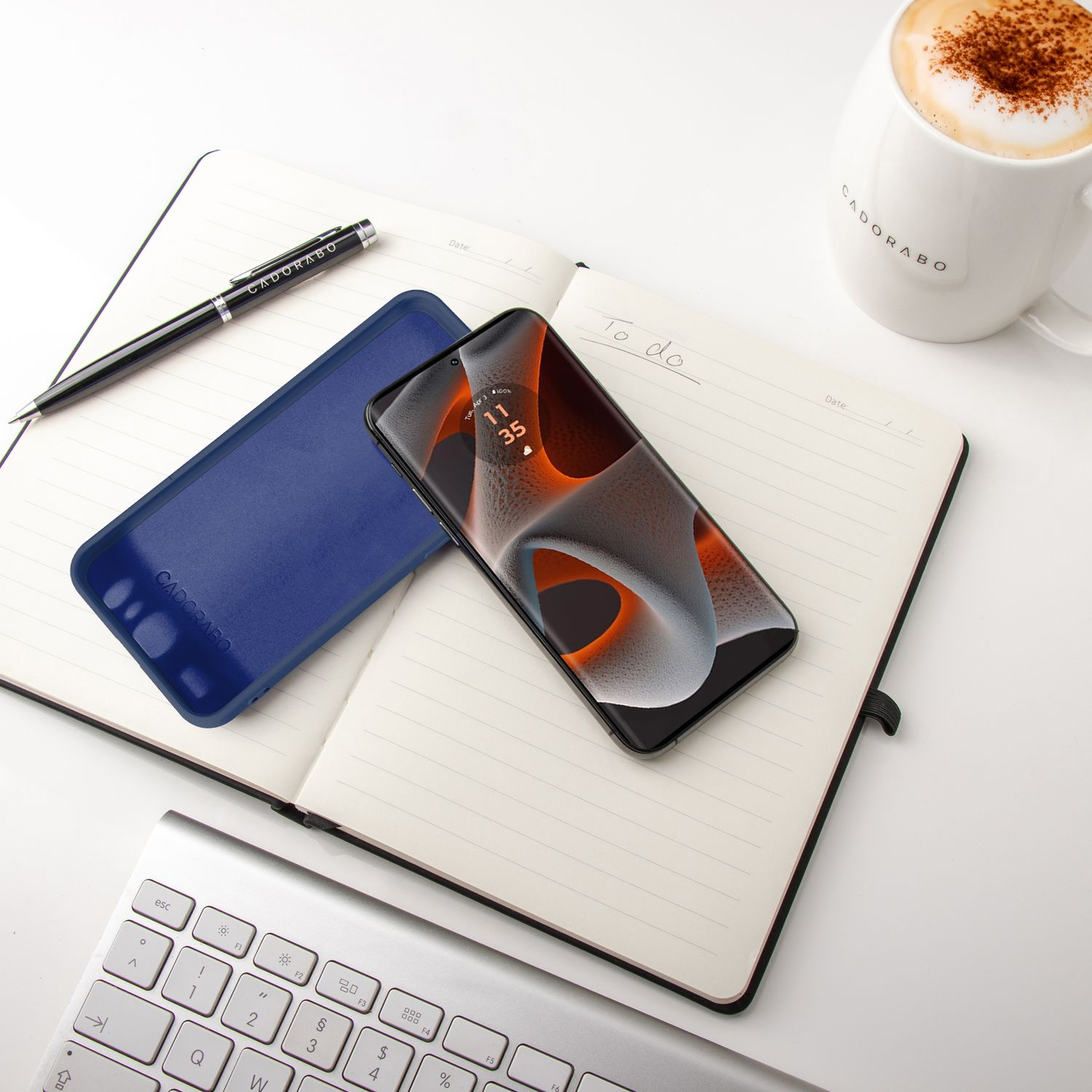 Notizbuch mit Telefon, Stift und Kaffeetasse auf weißer Oberfläche.