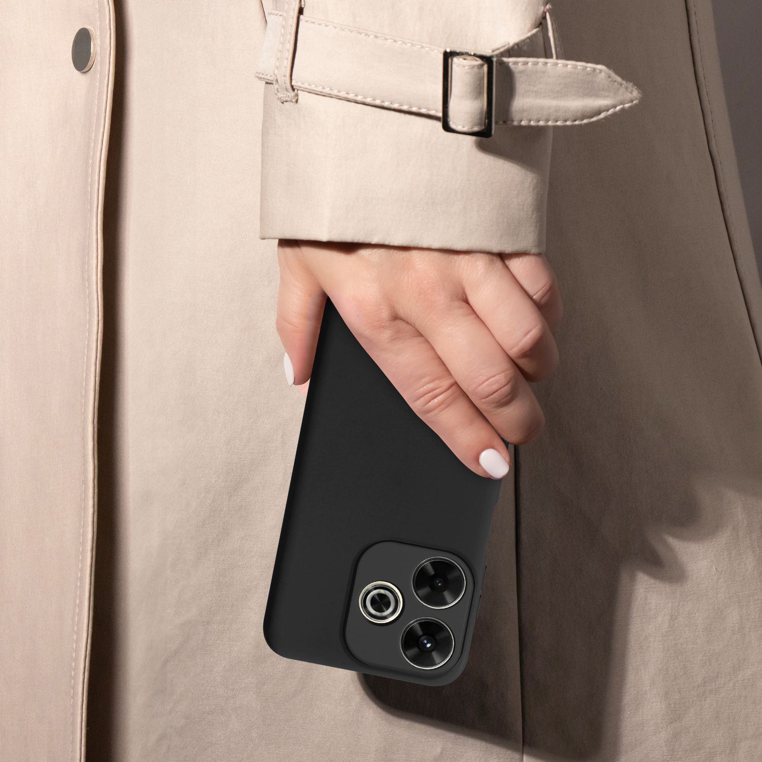 Eine Person in einem beigefarbenen Mantel hält ein schwarzes Telefon mit drei Kameras. Weißer Nagellack.
