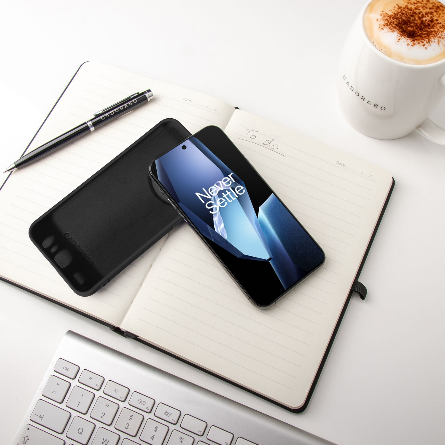 Ein Telefon, eine Hülle, ein Stift und eine Tasse auf einem offenen Notizbuch auf weißem Schreibtisch.