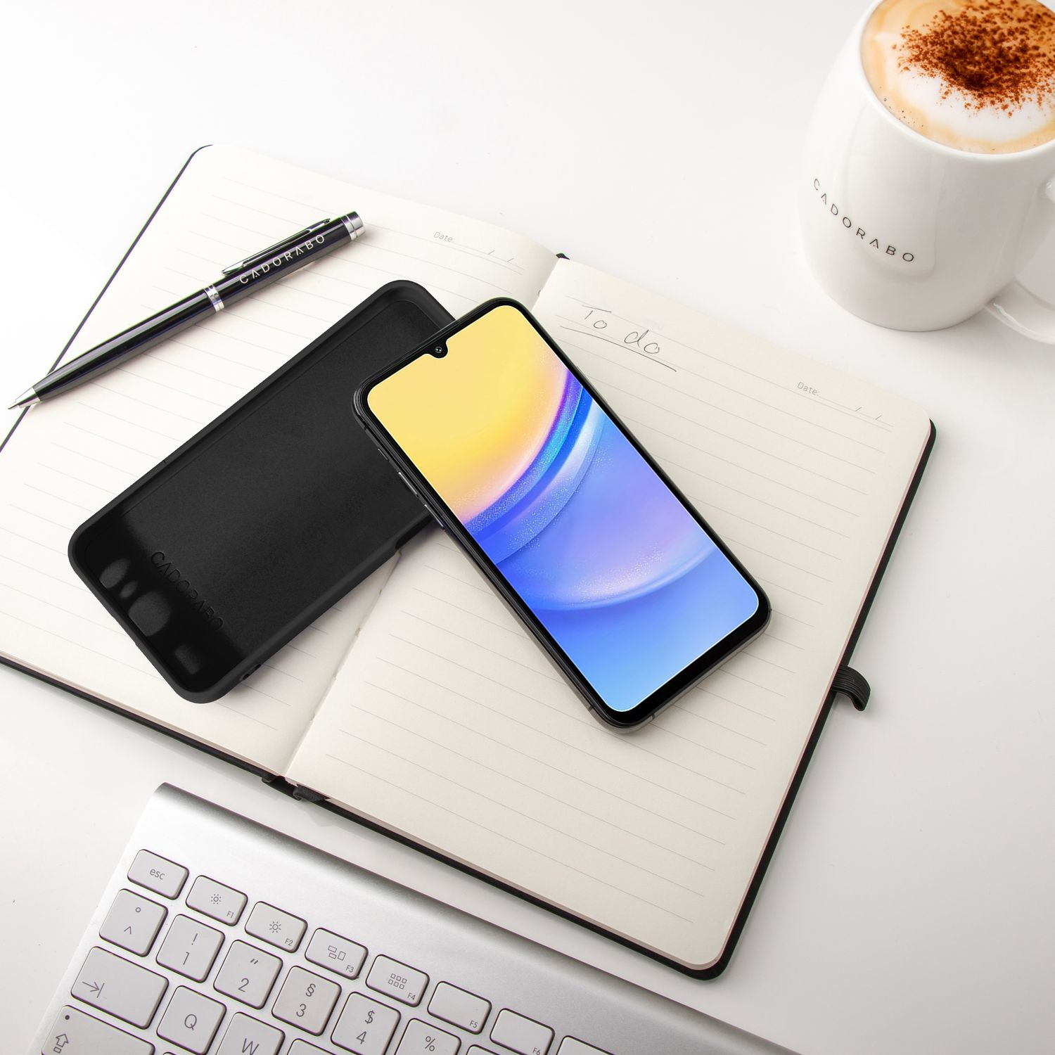 Telefon auf Notizbuch mit Stift und Kaffee. Daneben eine Handyhülle. Weißer Hintergrund.