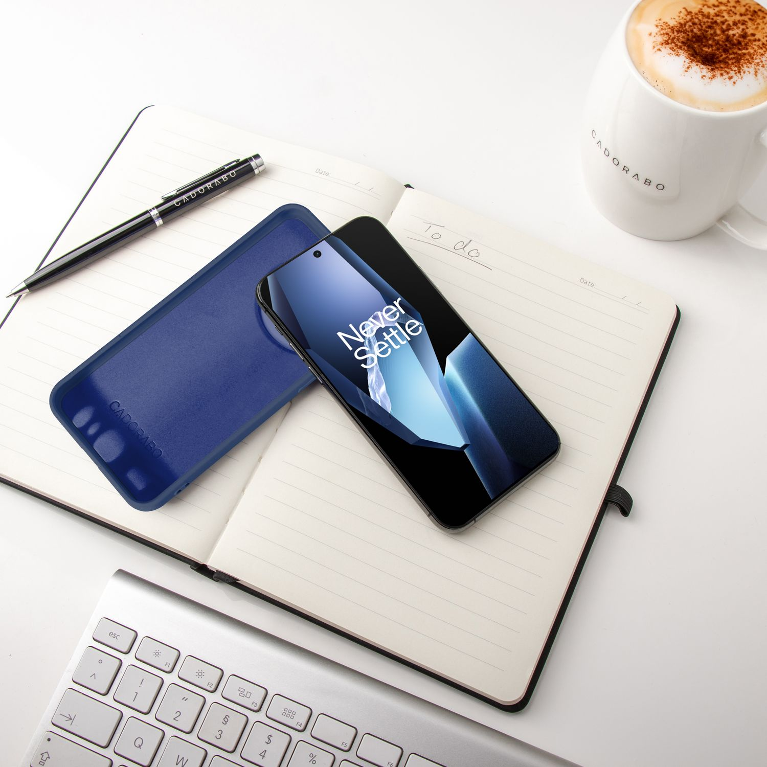 Telefon auf Notizbuch mit Stift und Kaffee. Daneben eine Handyhülle. Weißer Hintergrund.