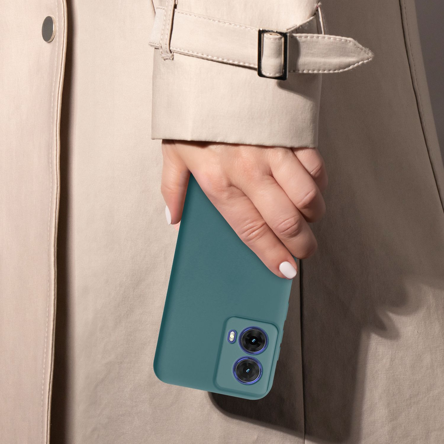 Eine Hand hält ein türkisgrünes Telefon mit zwei Kameras, trägt einen beigen Mantel.