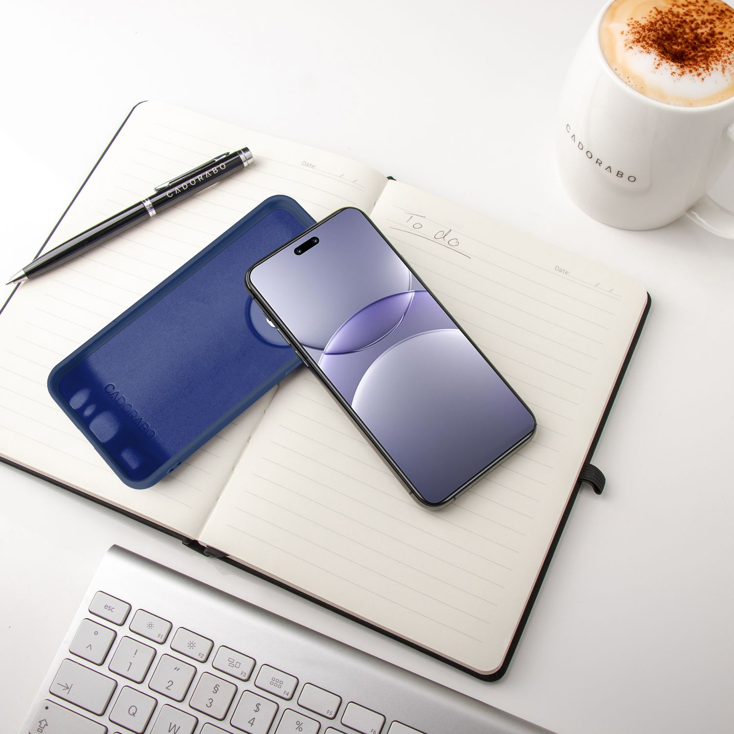 Ein Telefon und eine blaue Handyhülle auf einem Notizbuch neben einem Stift und einer Kaffeetasse.
