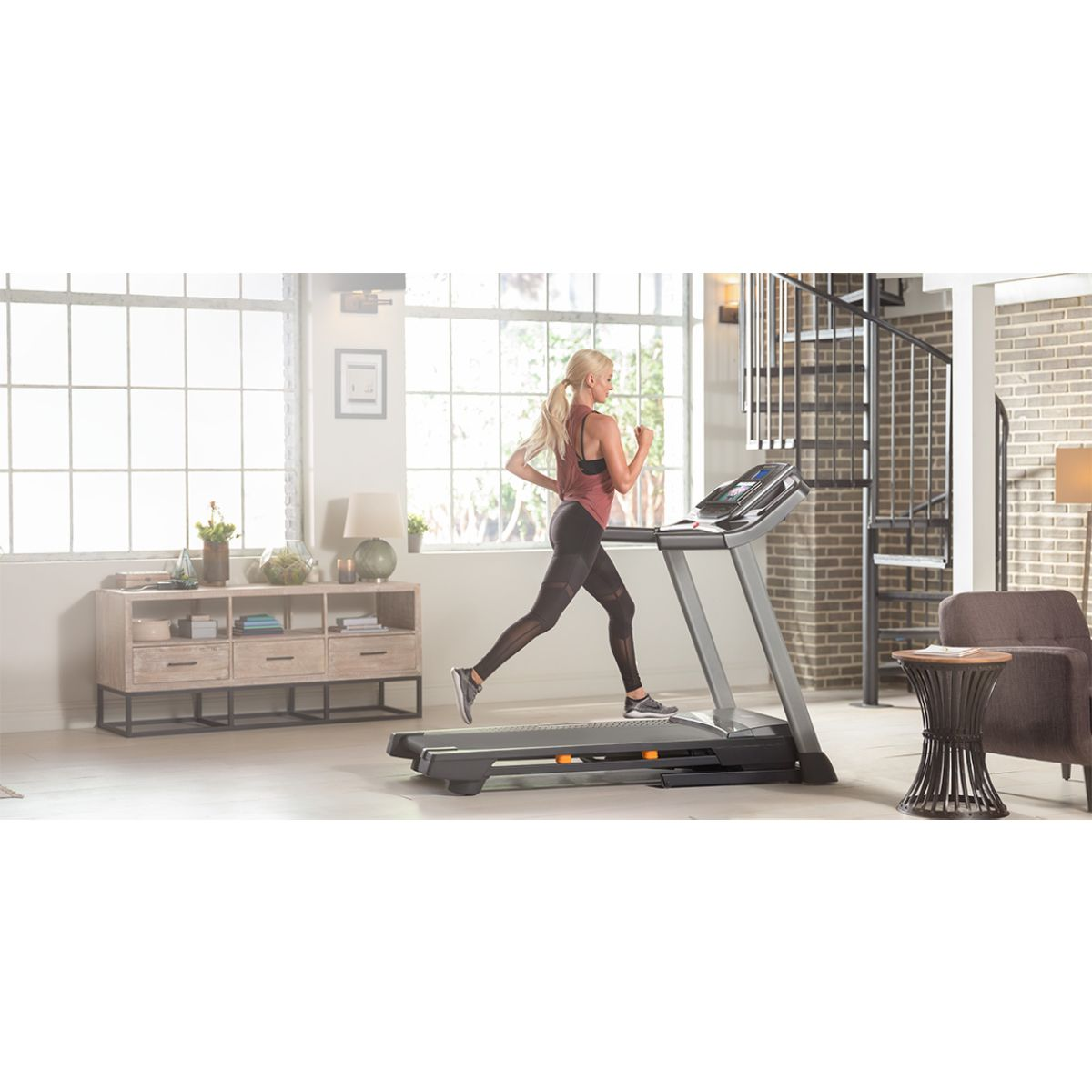 Frau läuft auf einem Laufband in einem Home-Gym. Innenraum mit Fenstern und Möbeln.