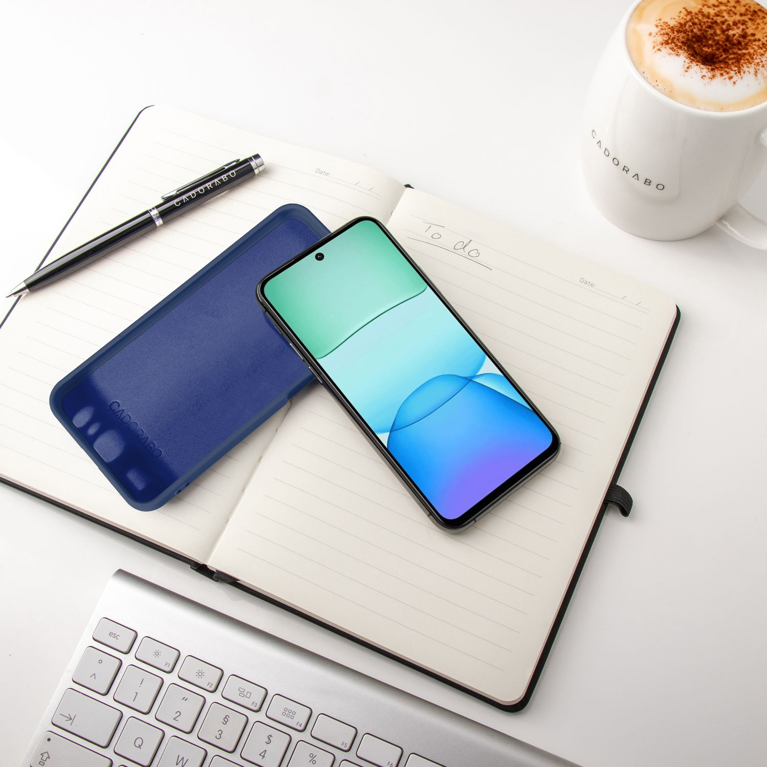 Telefon, Hülle, Stift und Kaffeetasse auf Notizbuch und Tastatur, weiße Oberfläche.