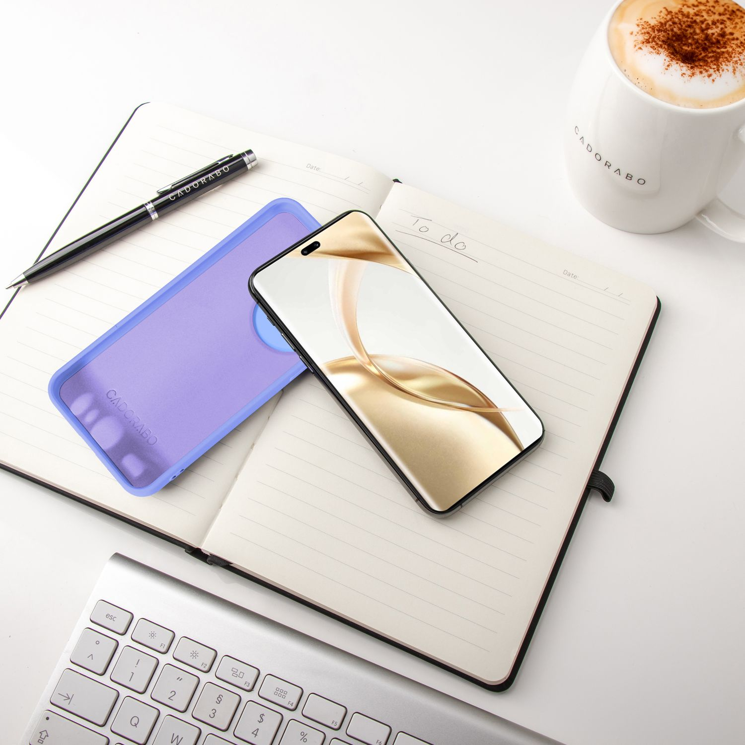 Ein Notizbuch, Telefon, Handyhülle, Stift und Kaffeetasse auf weißer Oberfläche. Das Telefon liegt auf dem Notizbuch.