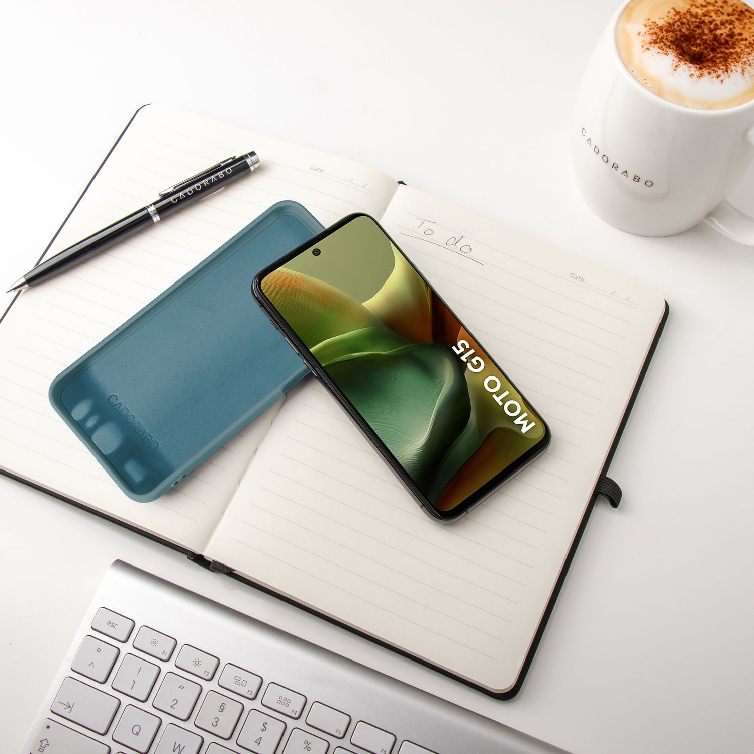 Notizbuch mit Telefon, Hülle und Stift auf weißer Oberfläche. Telefon zeigt grünen Hintergrund.