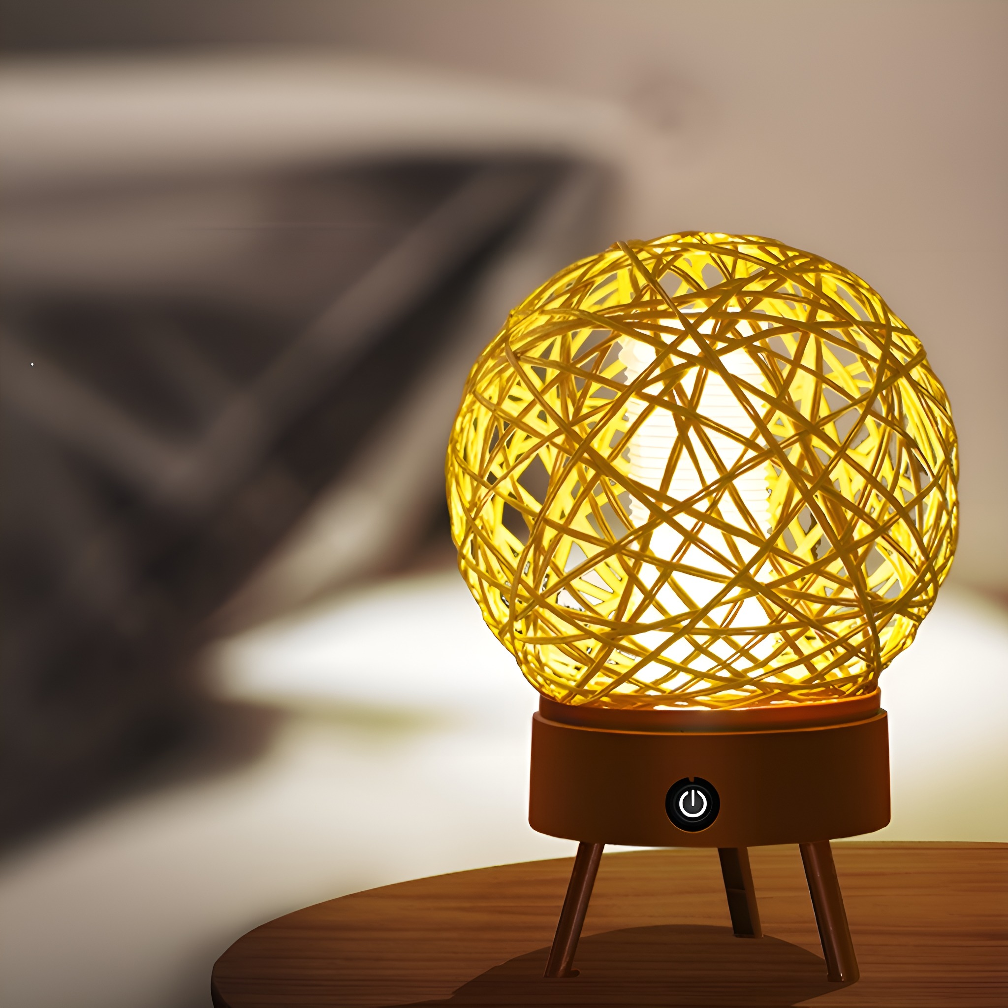 Eine gelbe, kugelförmige Lampe aus gewebtem Material, auf einem braunen Sockel mit drei Beinen und einem Ein-/Ausschalter.