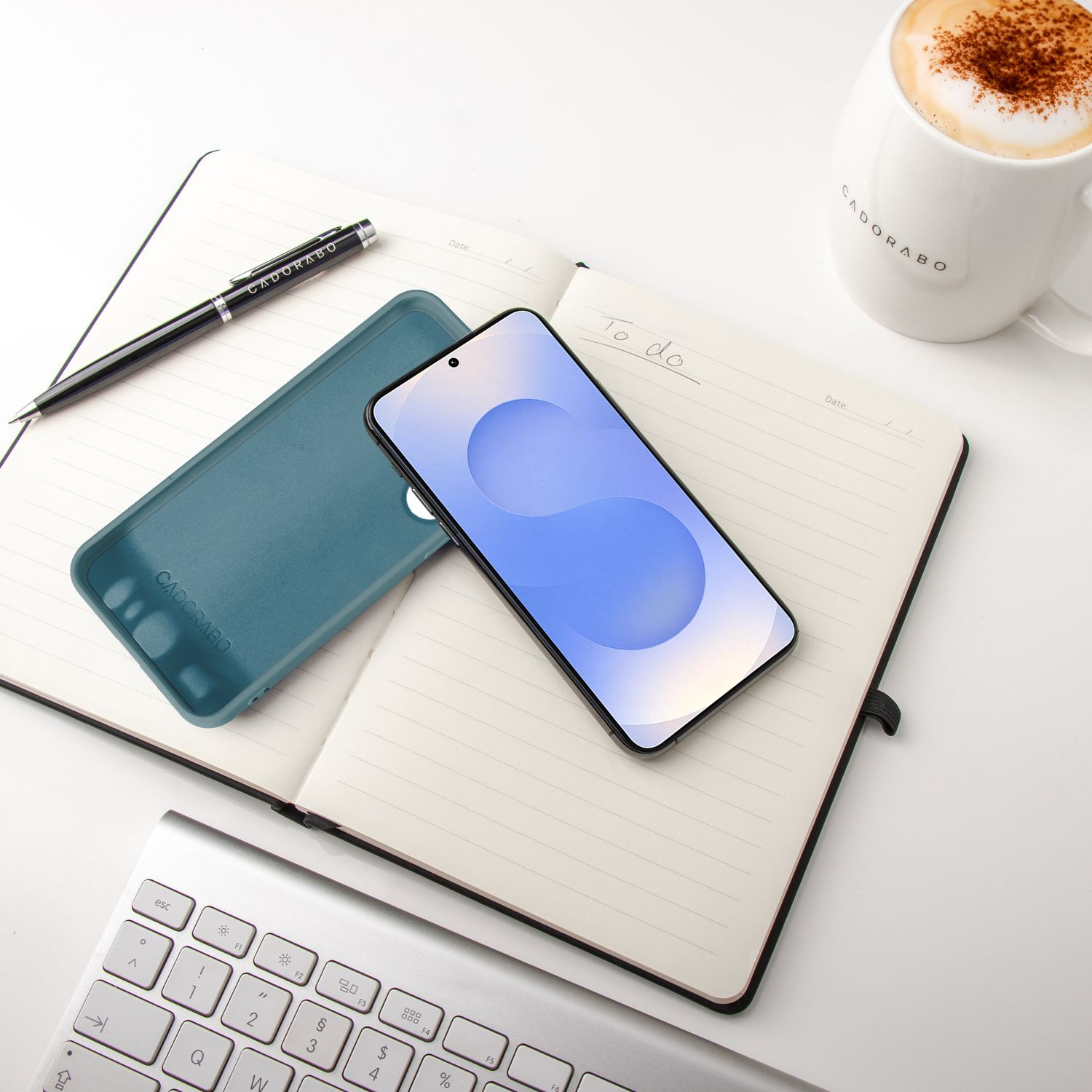Ein Telefon, eine Handyhülle, ein Stift, ein Notizbuch und eine Kaffeetasse auf einer weißen Oberfläche.