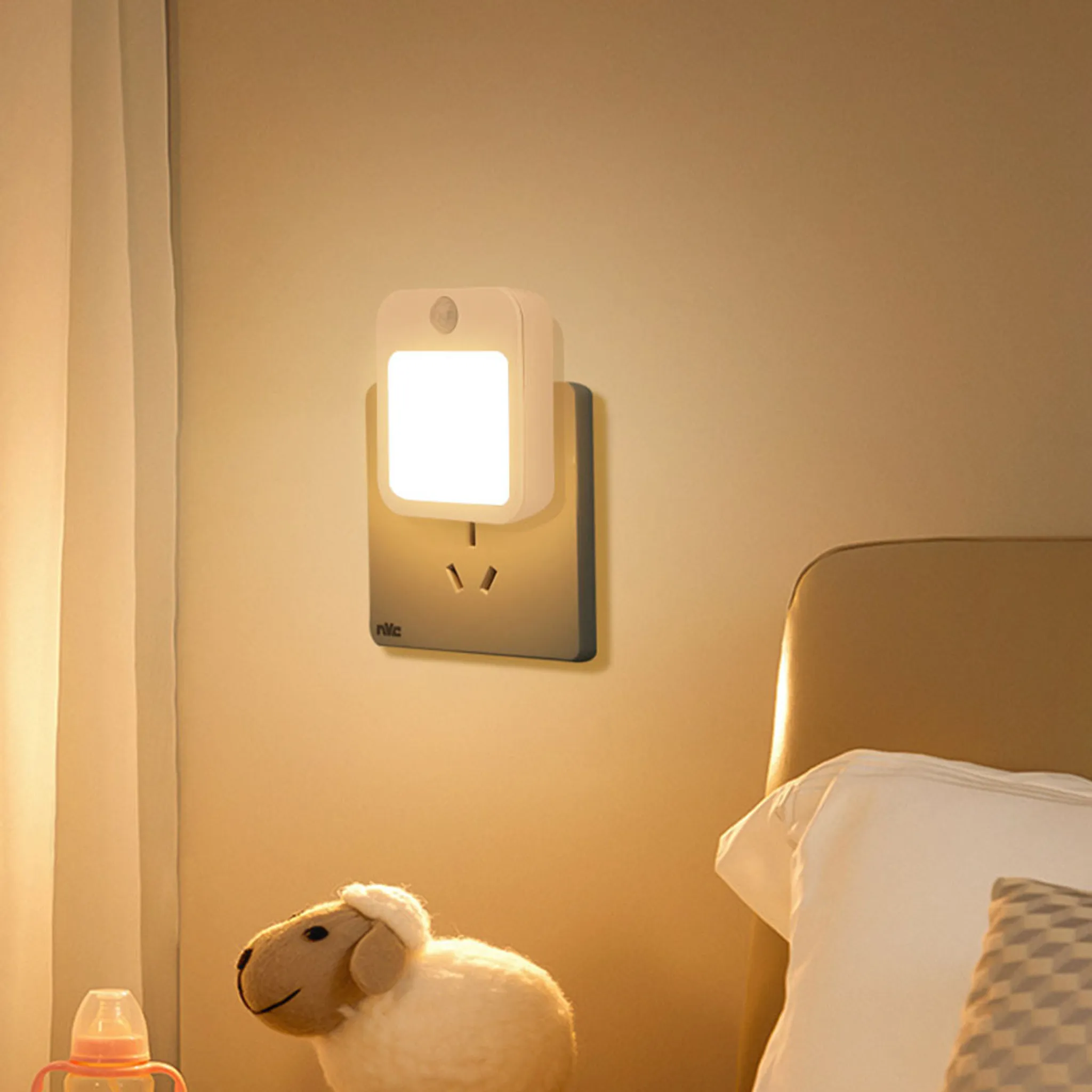 Ein kleines weißes Nachtlicht in einer Steckdose. Ein Stoffschaf liegt auf dem Bett.