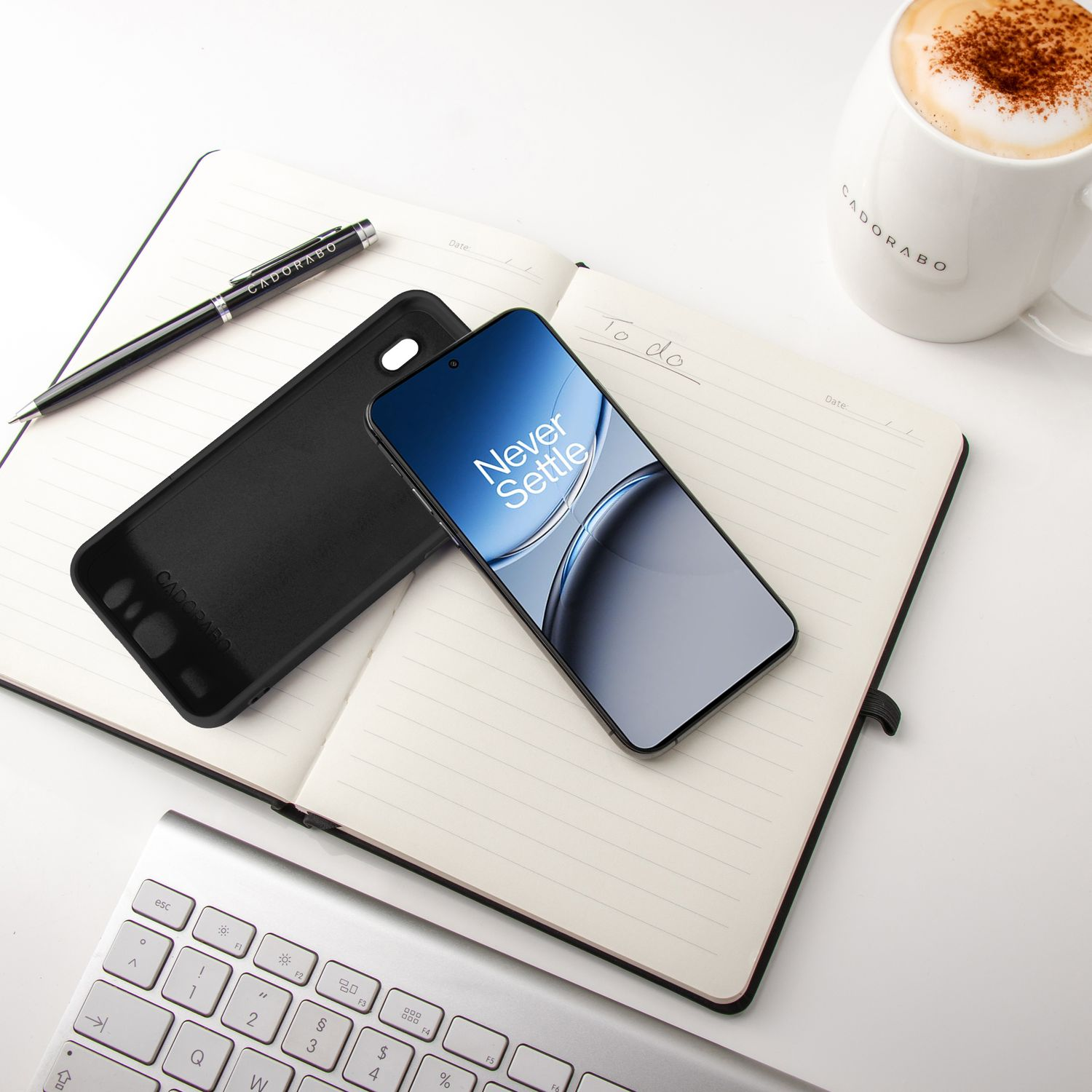 Ein Telefon und eine Hülle auf einem Notizbuch, mit Stift und Becher. Tastatur sichtbar.