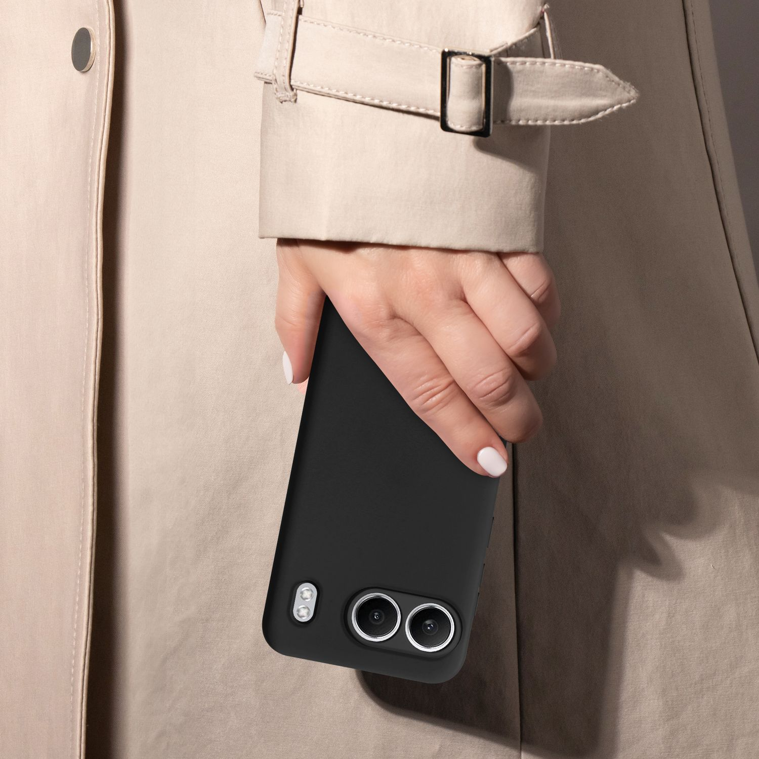 Person hält schwarzes Telefon in schwarzer Hülle, trägt beigefarbenen Trenchcoat.