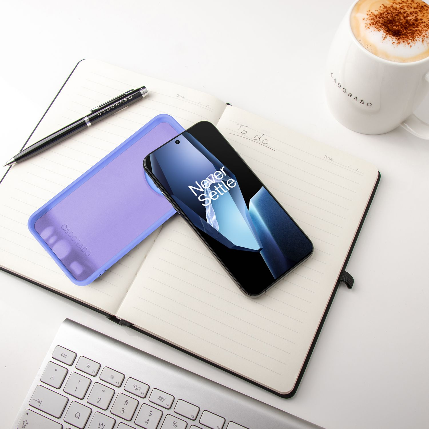 Notizbuch mit Telefon und Hülle. Stift und Becher liegen auf dem weißen Schreibtisch.