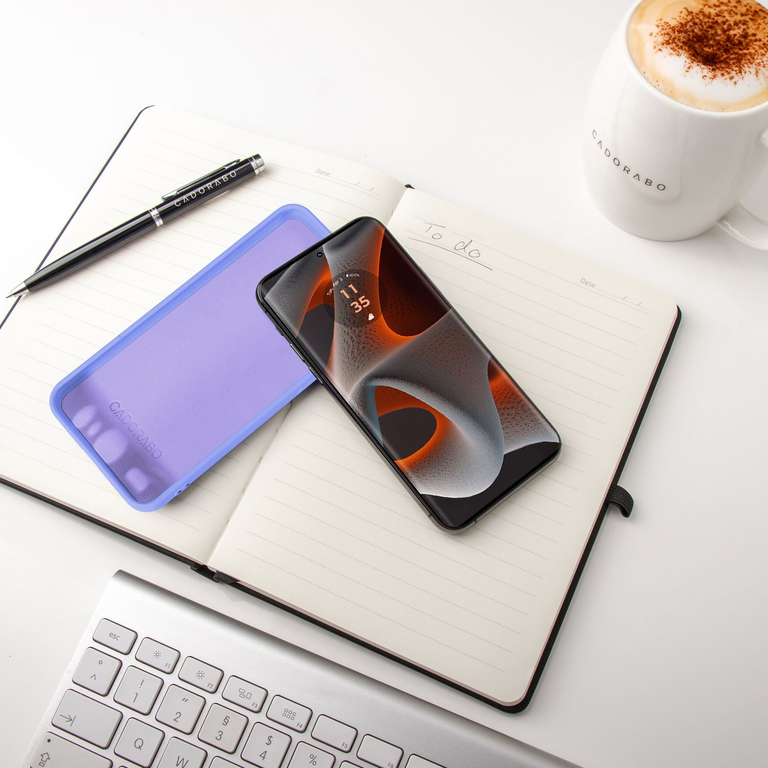 Ein Telefon auf einem Notizbuch mit Stift und Hülle. Im Hintergrund steht eine Kaffeetasse.